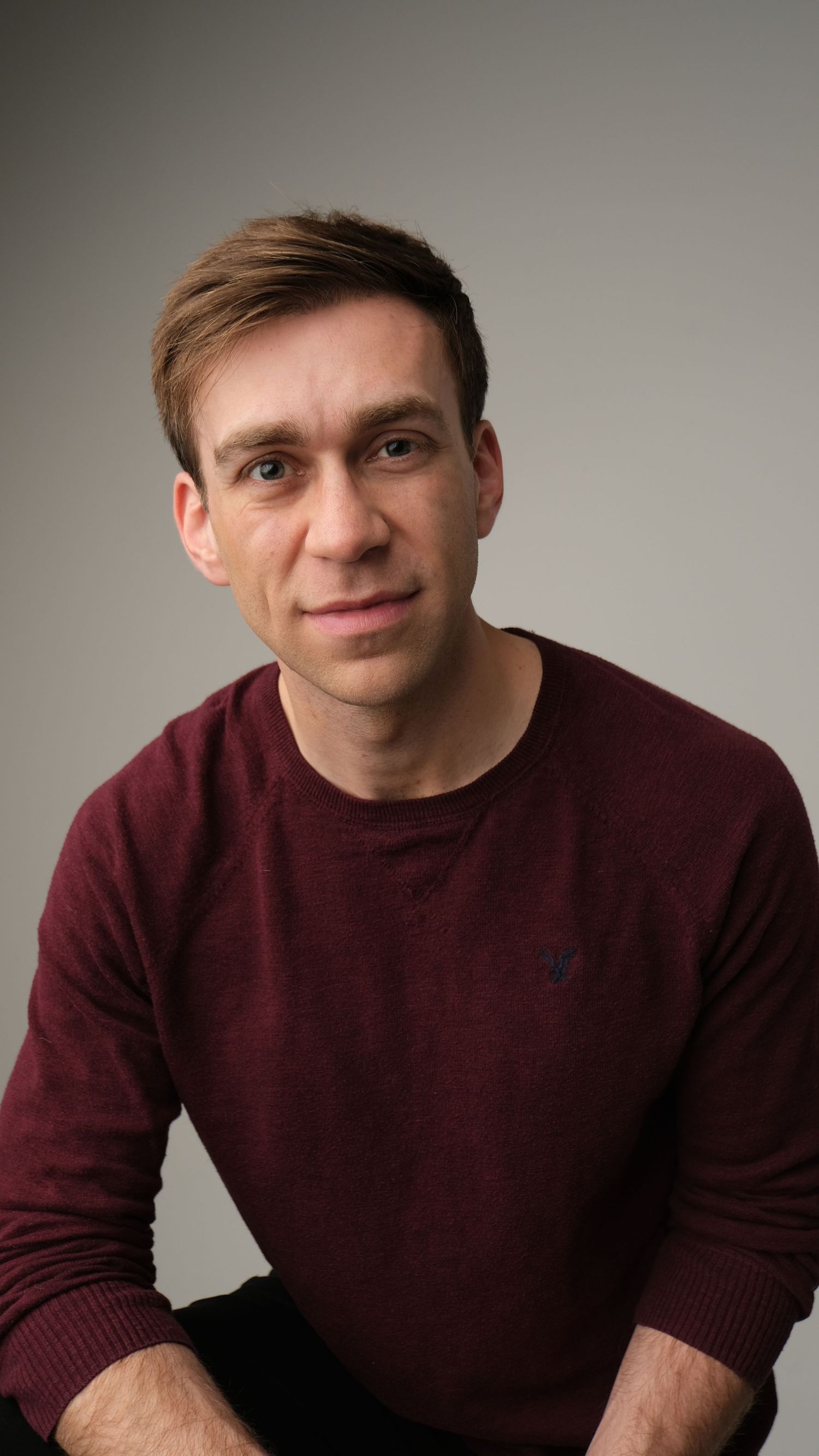 Portrait in burgundy sweater against neutral studio backdrop showing casual style.
