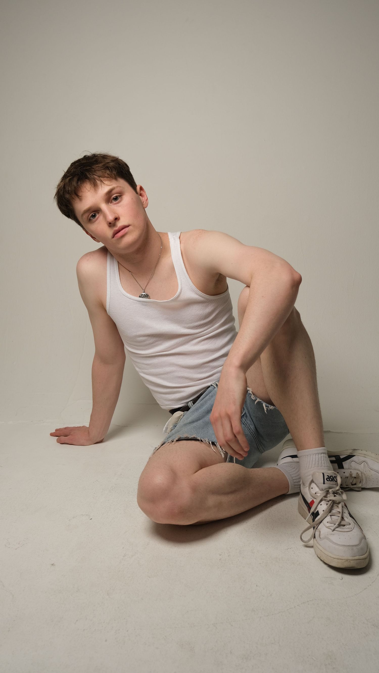 A person in white tank top and denim shorts reclines on a light colored floor.