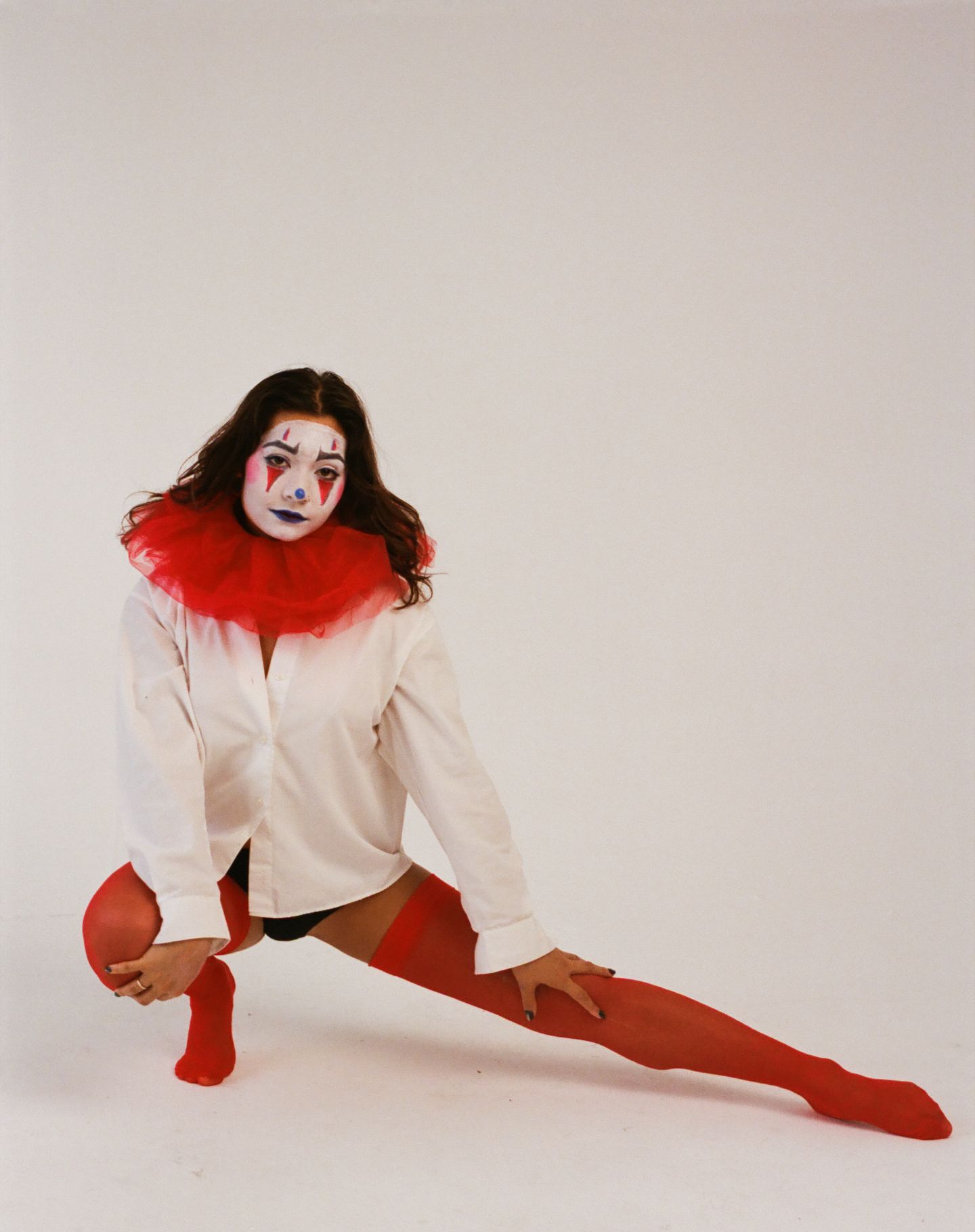 Performer in white costume with clown makeup strikes dramatic poses against white backdrop in artistic photo series.