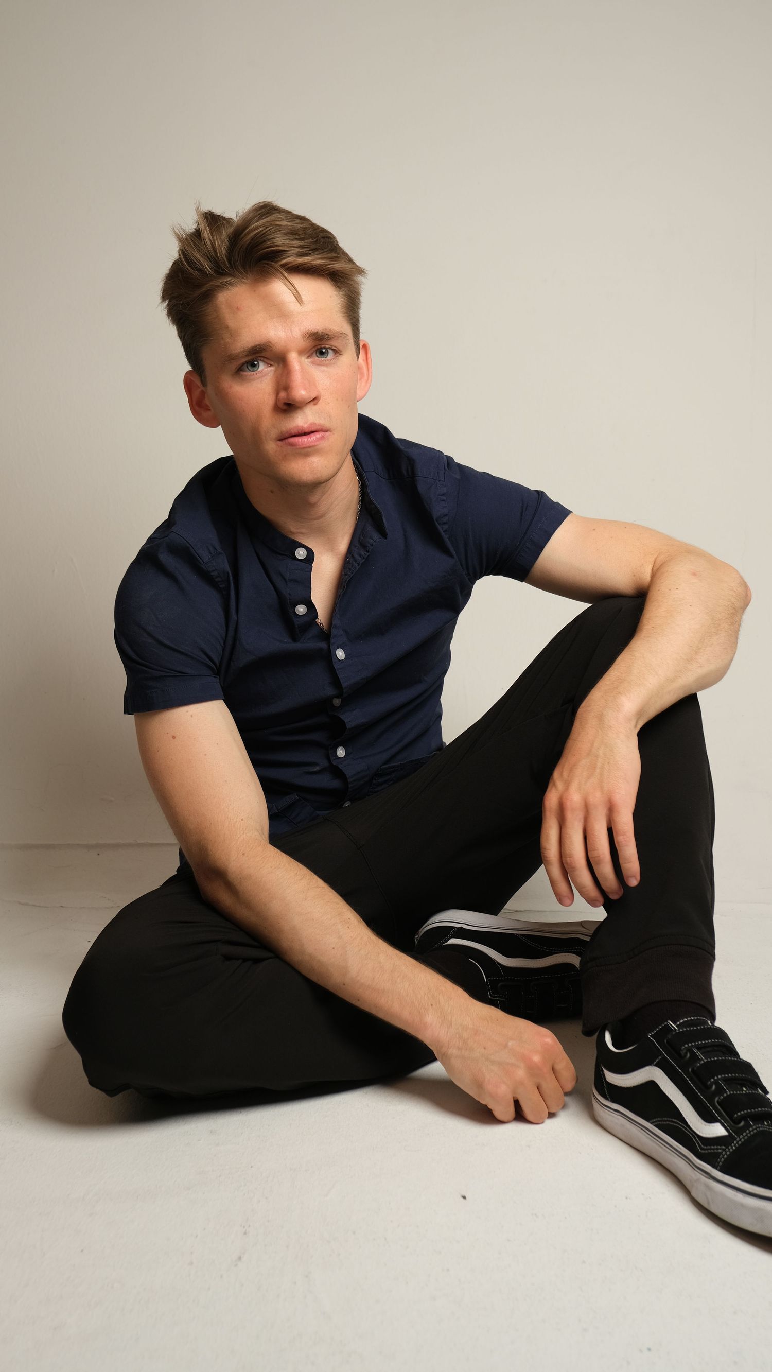 Casual portrait series showing a person in a navy polo shirt reclining on a light floor.