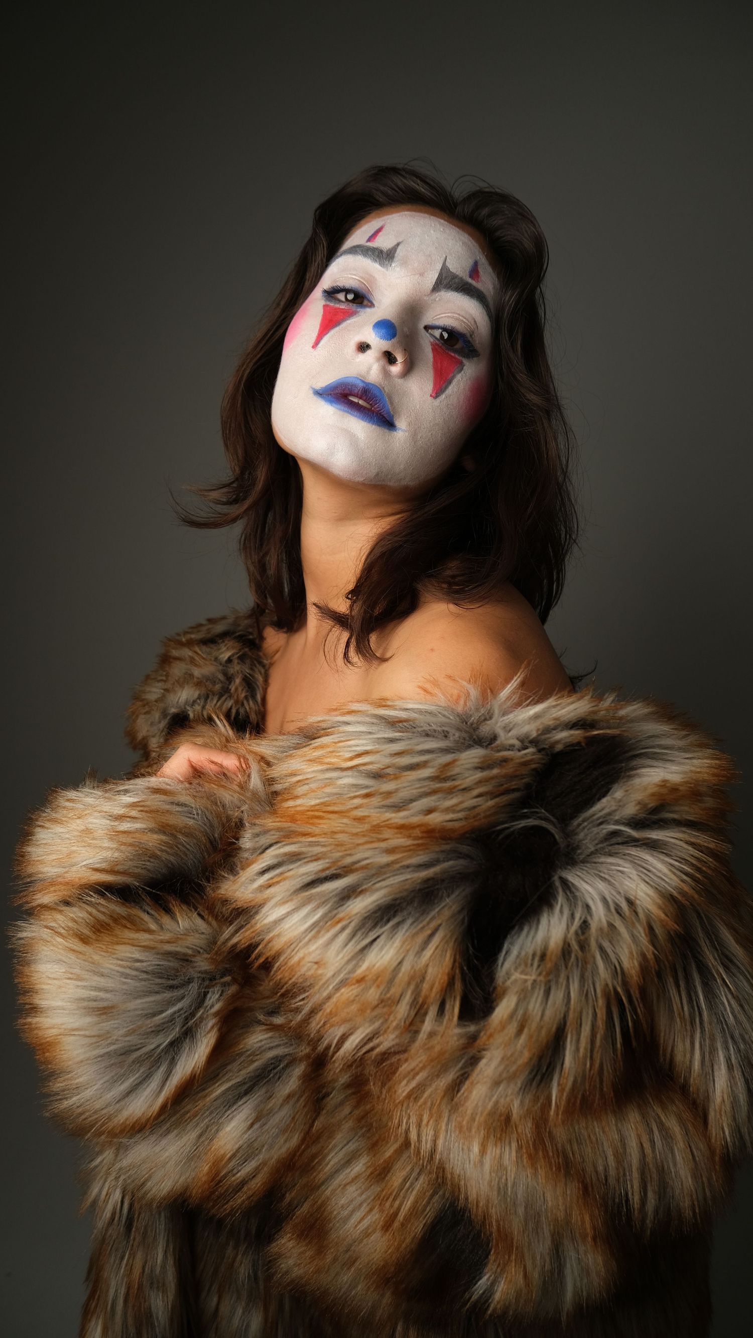 Dramatic portrait featuring white face paint and red accents against dark background with brown fur collar.