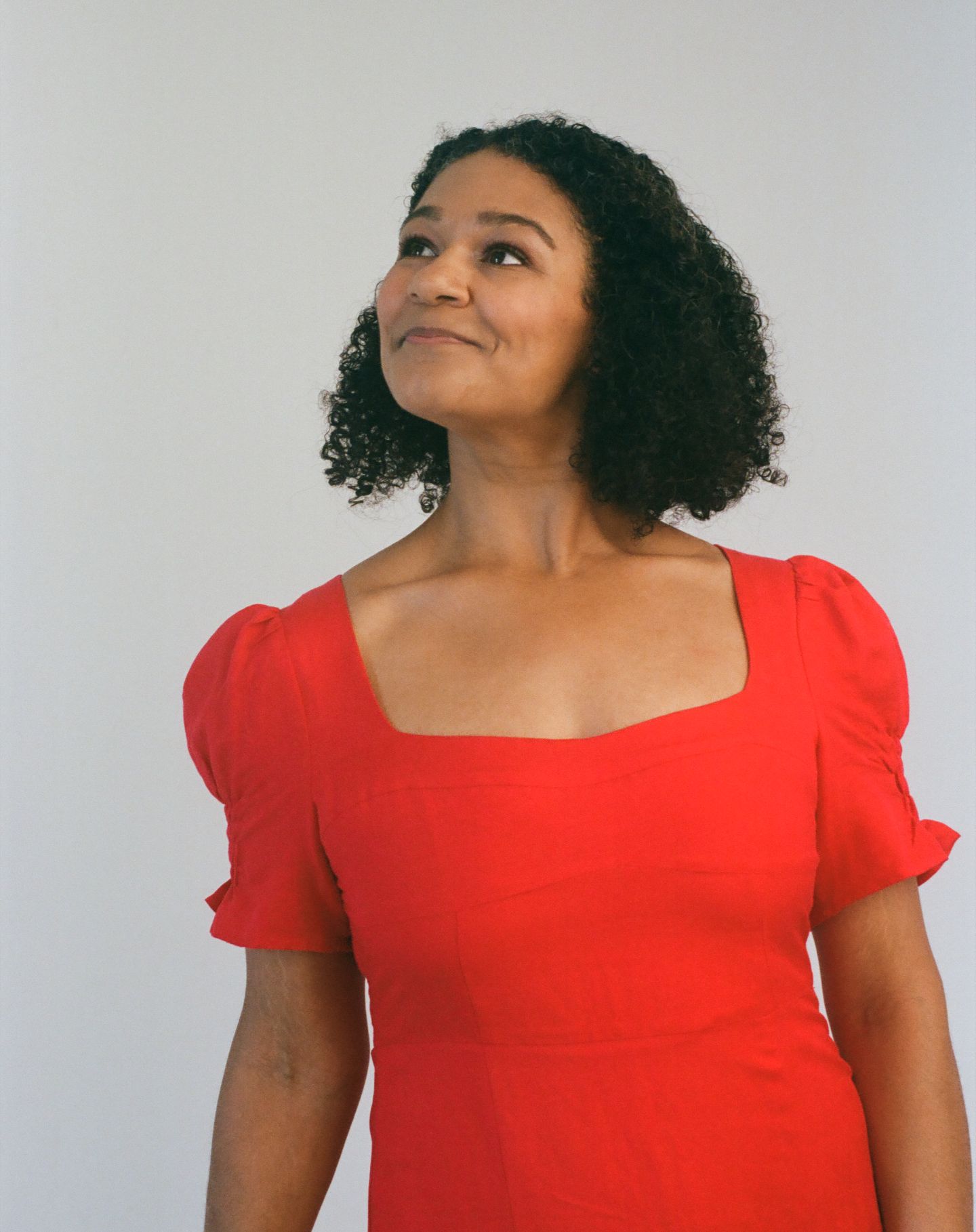 Someone in a vibrant red dress with puff sleeves and natural curly hair poses gracefully in a studio setting.