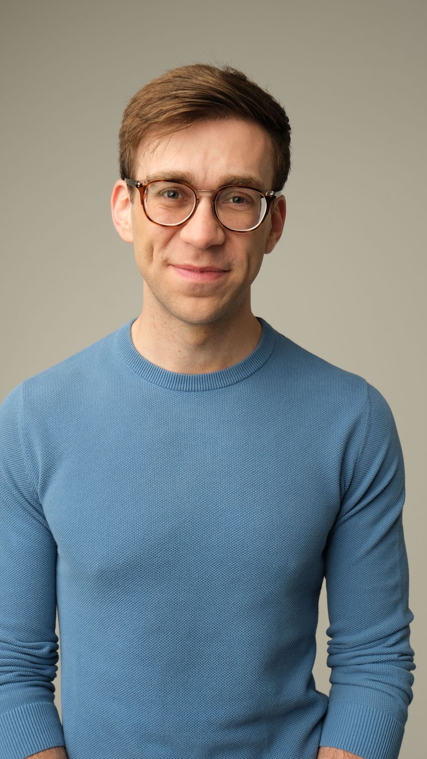 Portrait of a person wearing glasses and a light blue sweater against a neutral background.