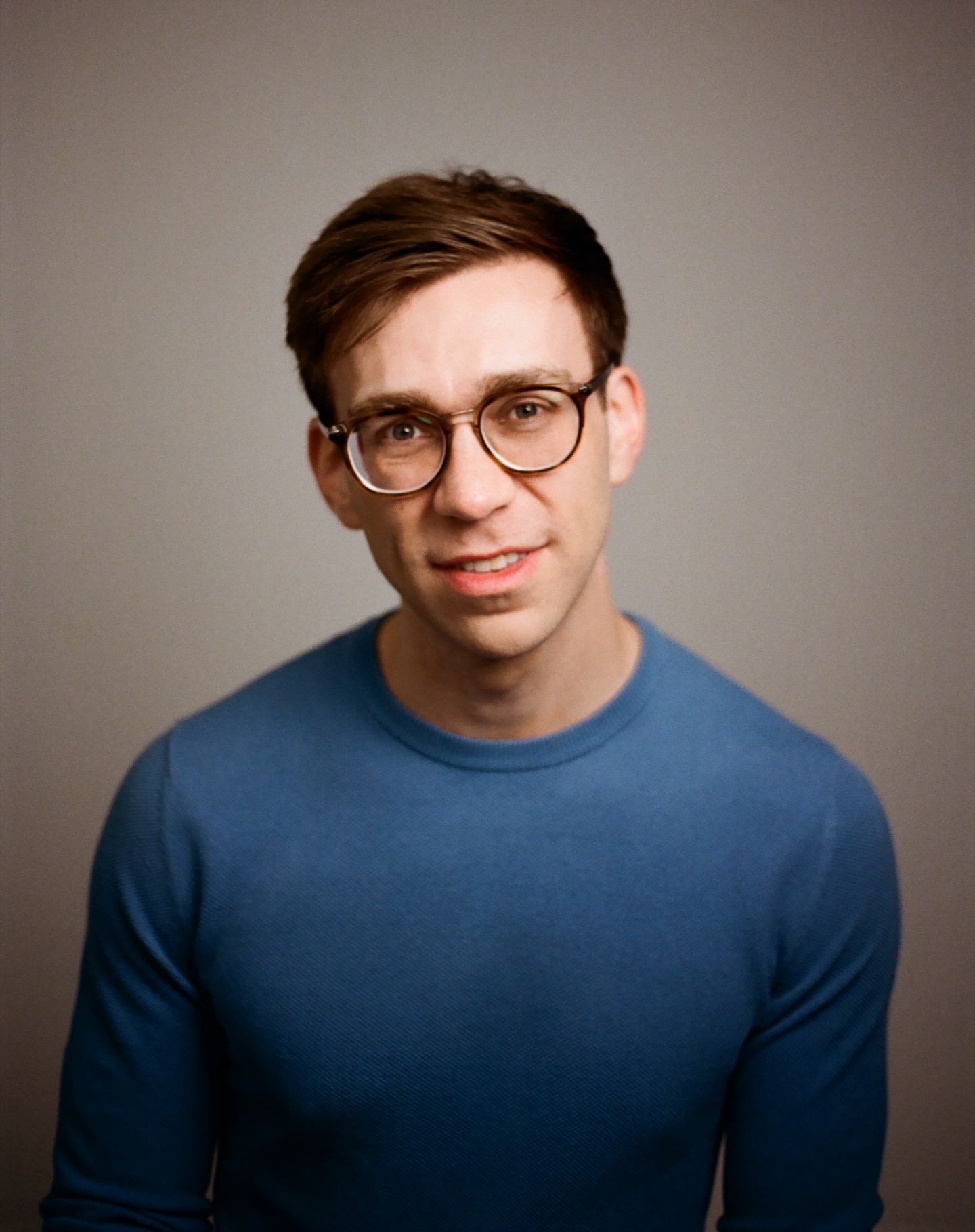 Series of studio portraits of a person in a blue sweater and glasses smiling against a neutral wall background.