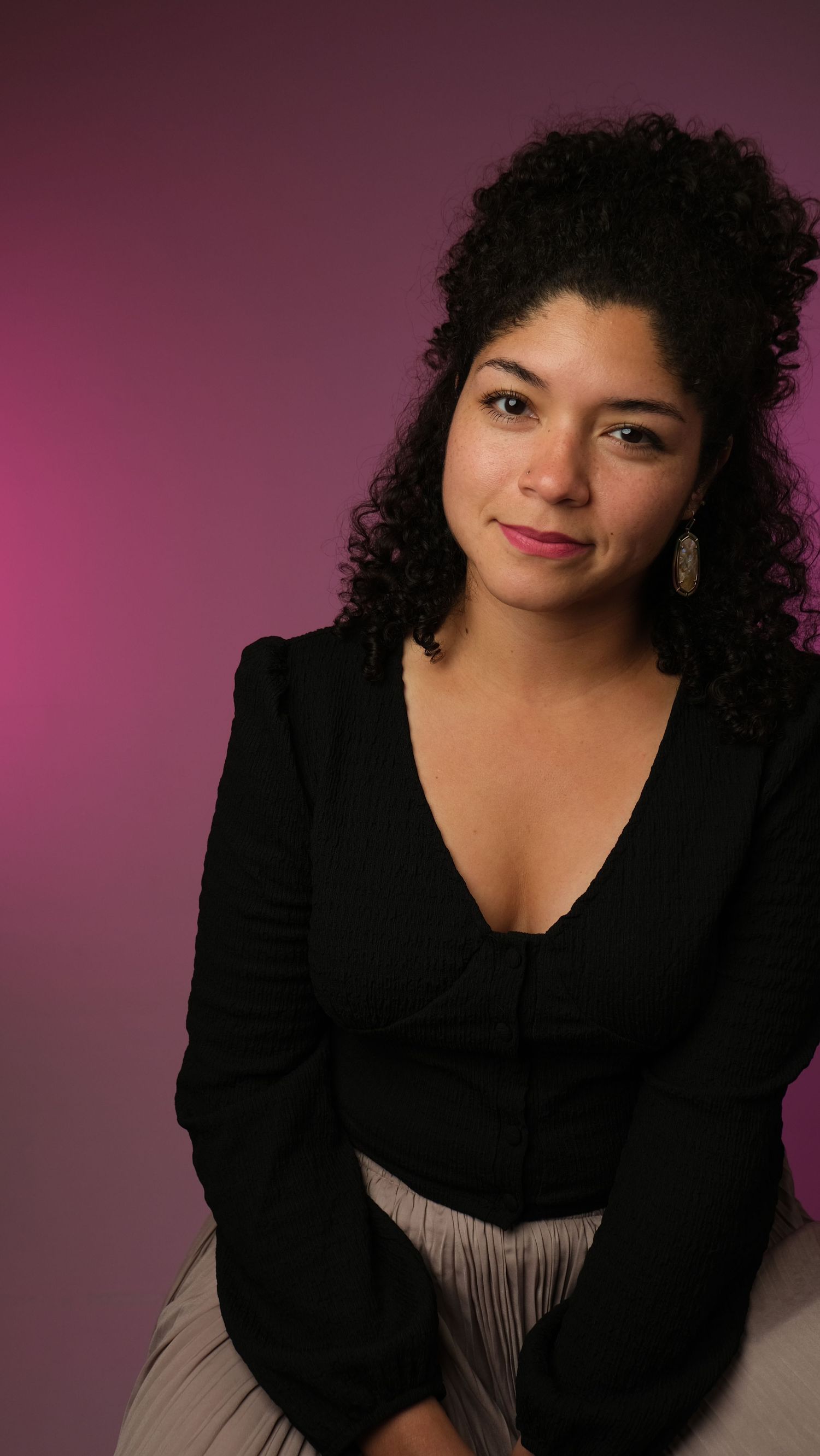 Portrait of a person in black blazer with curly hair against purple backdrop.