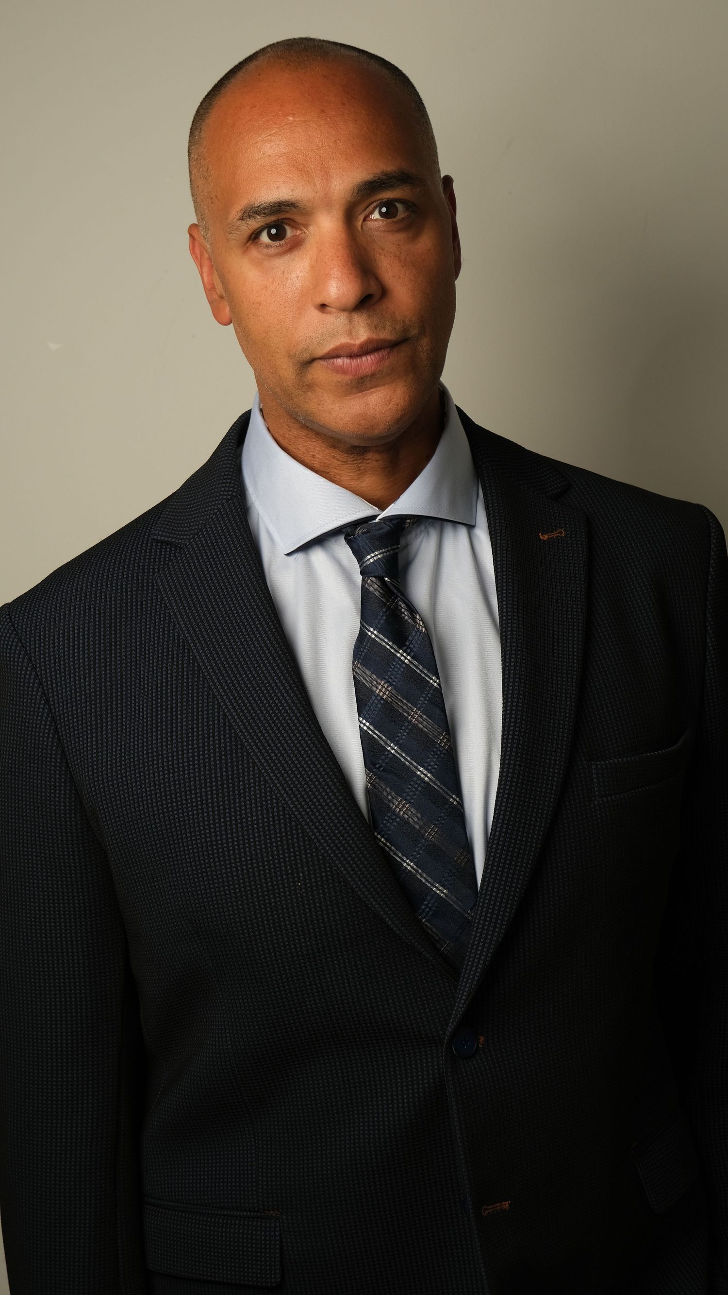 Professional headshot of a man in business attire with pinstriped suit and striped tie against a neutral backdrop.