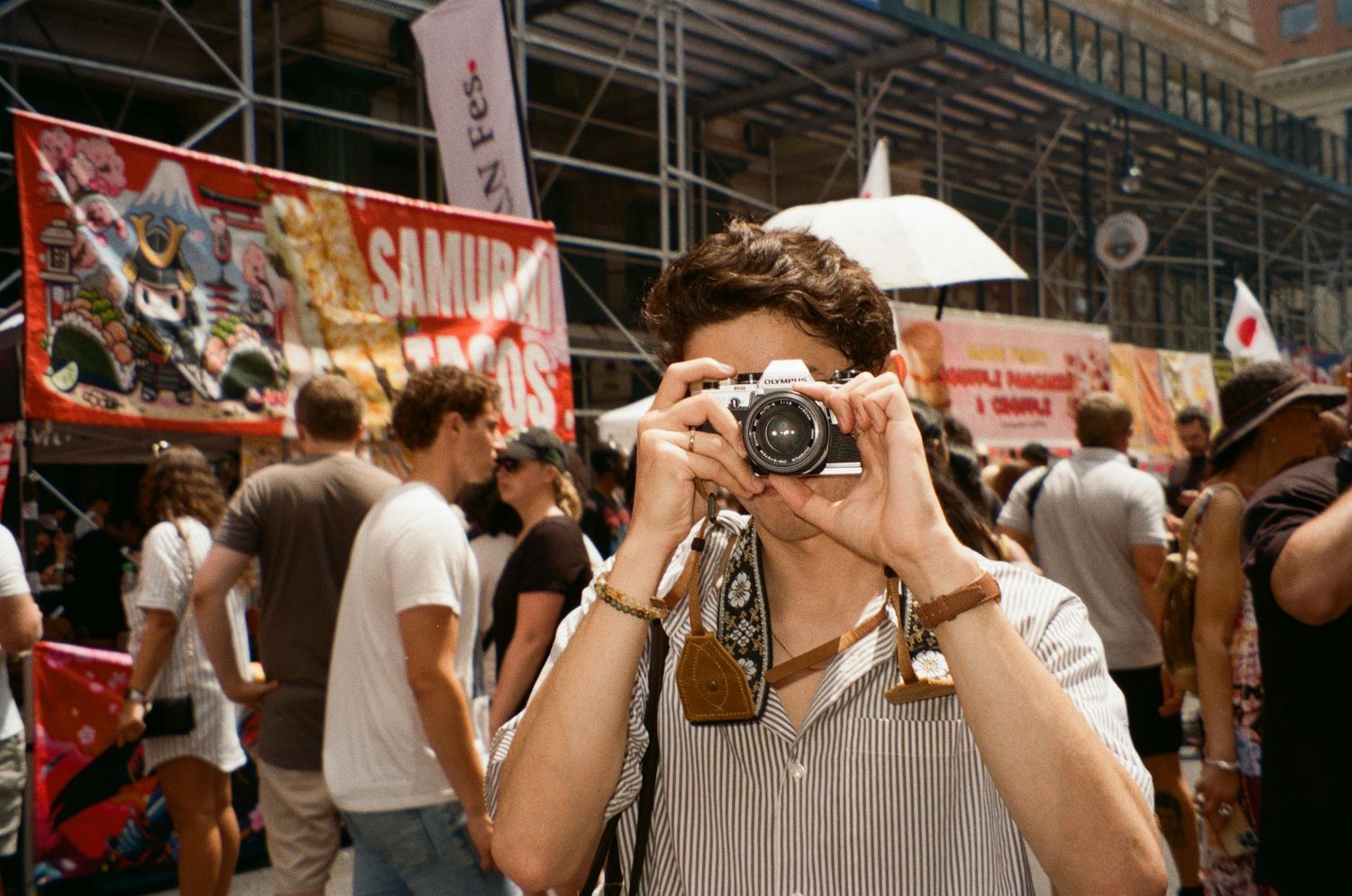 A crowd of people in sunlit urban setting holding up cameras and phones to take photos.