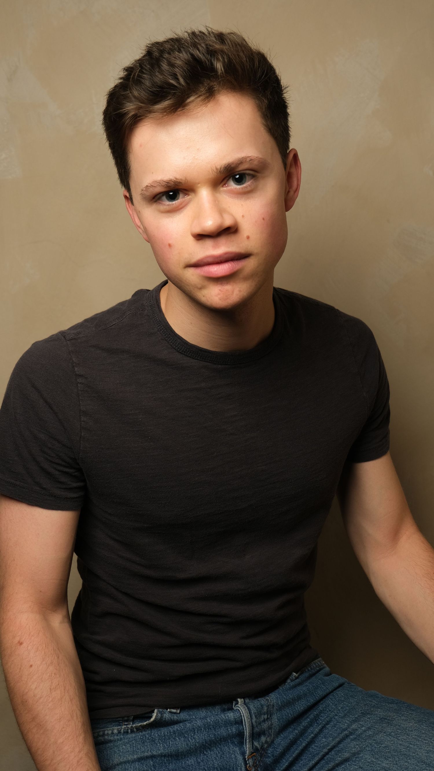 Portrait of a young person in a black t-shirt against a brown background in a casual pose.