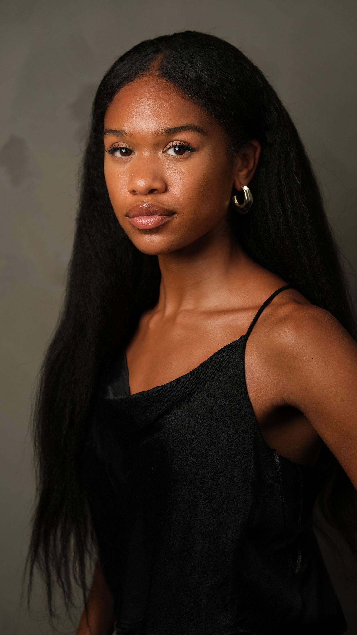 Professional portrait in black tank top against dark background showcasing long straight black hair and glowing skin.