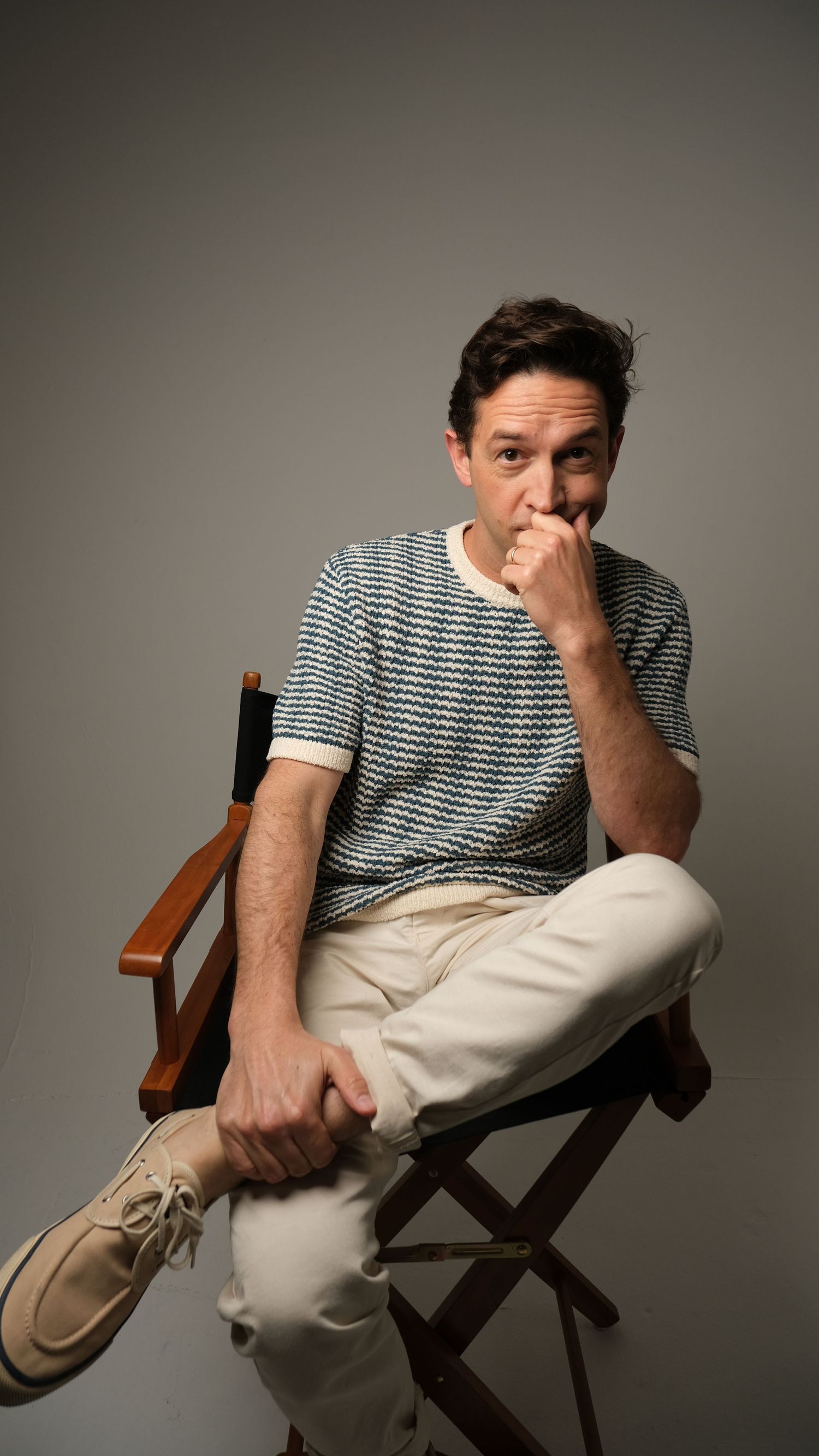 Candid studio shots of someone seated in director's chair wearing striped shirt and light colored pants.