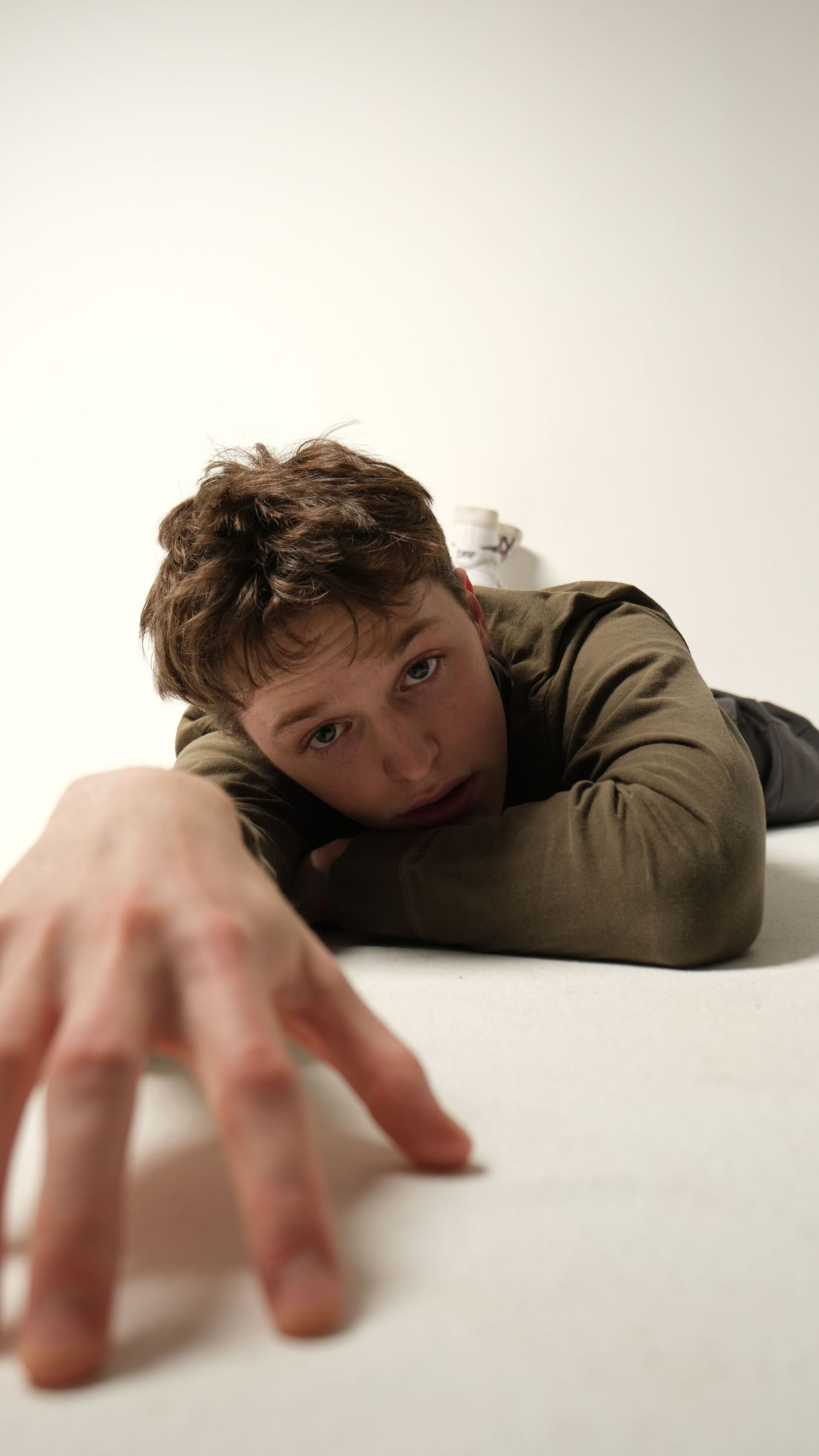 Dramatic lying down pose with hand reaching towards camera on white background.