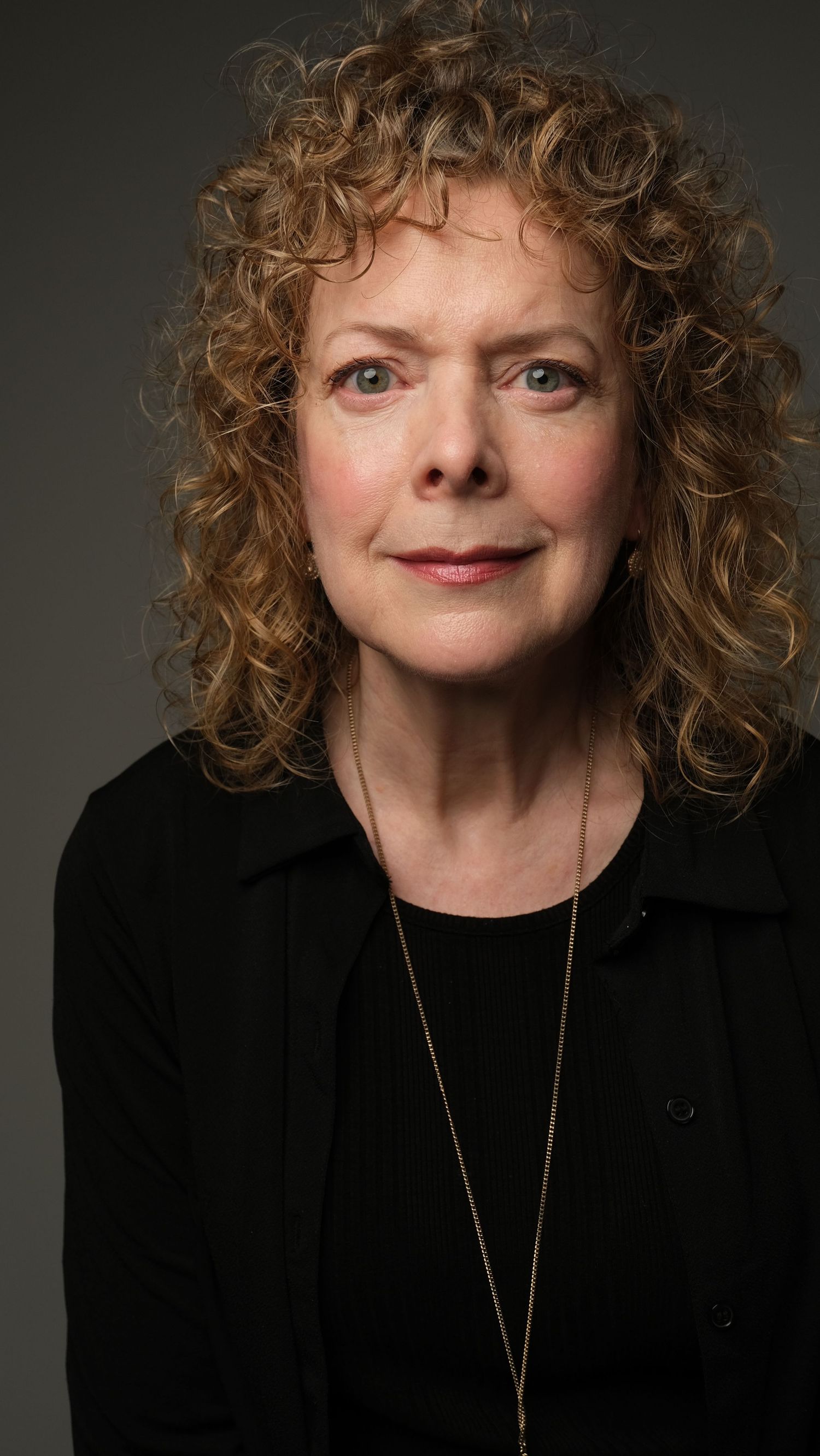 Professional headshot against dark backdrop wearing black clothing and delicate necklace.