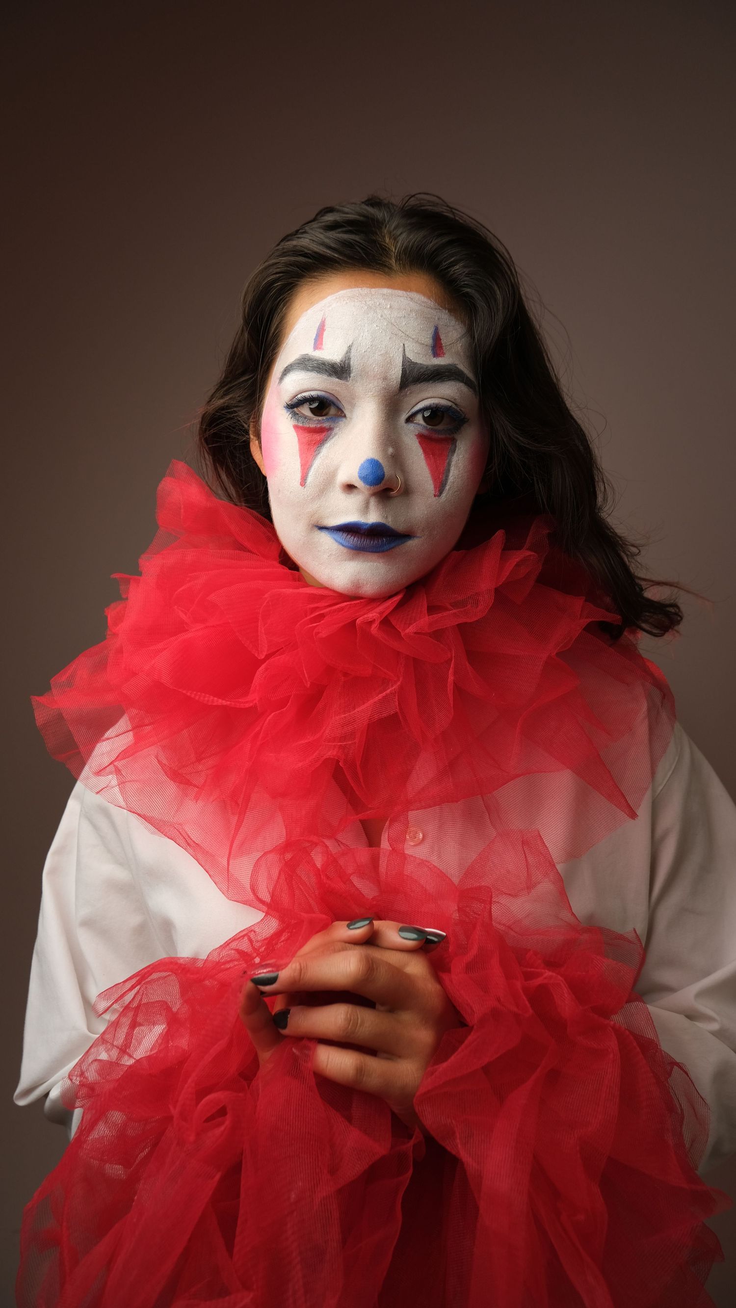 A figure in clown makeup and a bright red tulle collar poses dramatically against a dark background.