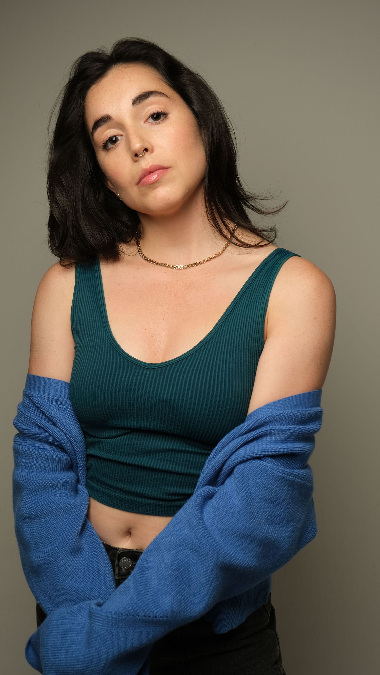 Fashion portrait featuring dark tank top and blue cardigan against neutral background, showcasing modern casual style.