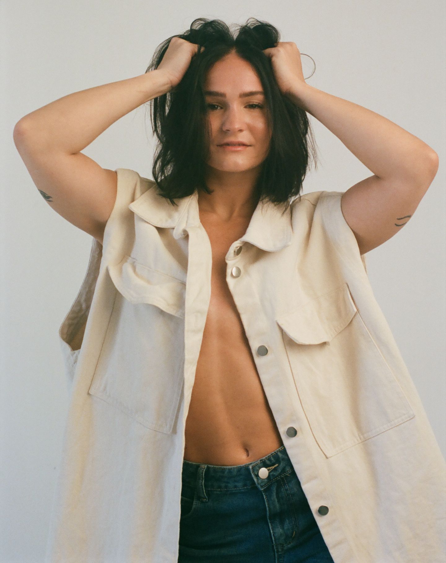 Fashion model in cream colored button-up shirt and dark denim jeans poses against white backdrop in photo series.