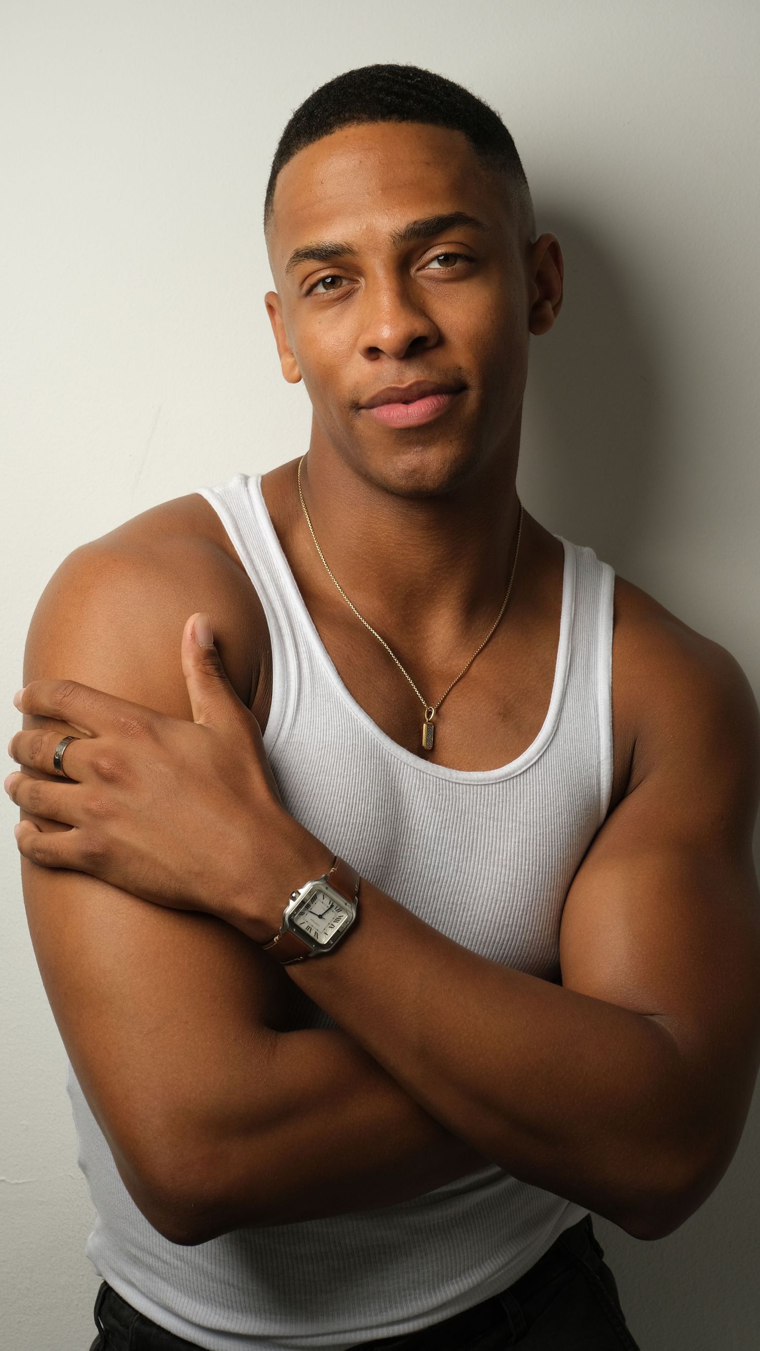 Athletic figure in white tank top poses confidently against neutral backdrop.