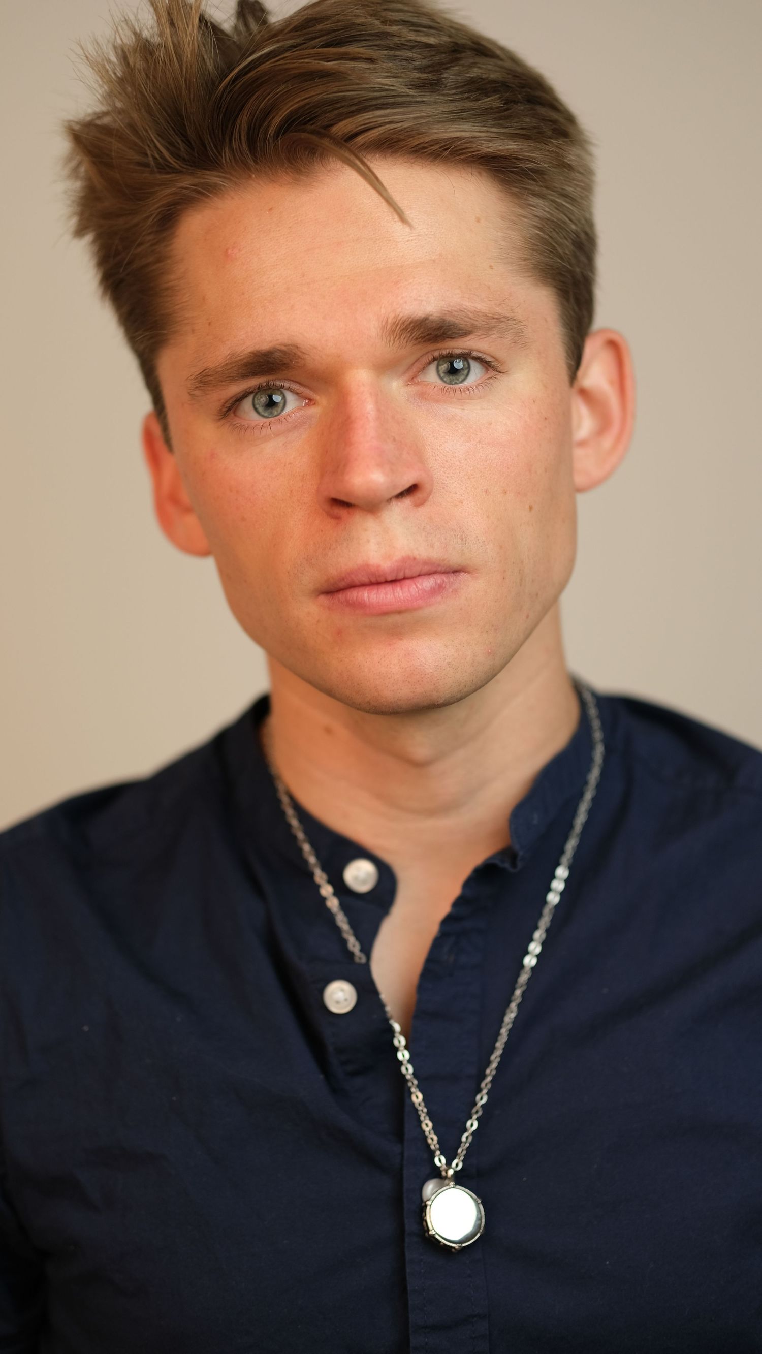 Studio headshots featuring casual navy shirt and silver necklace against neutral backdrop.