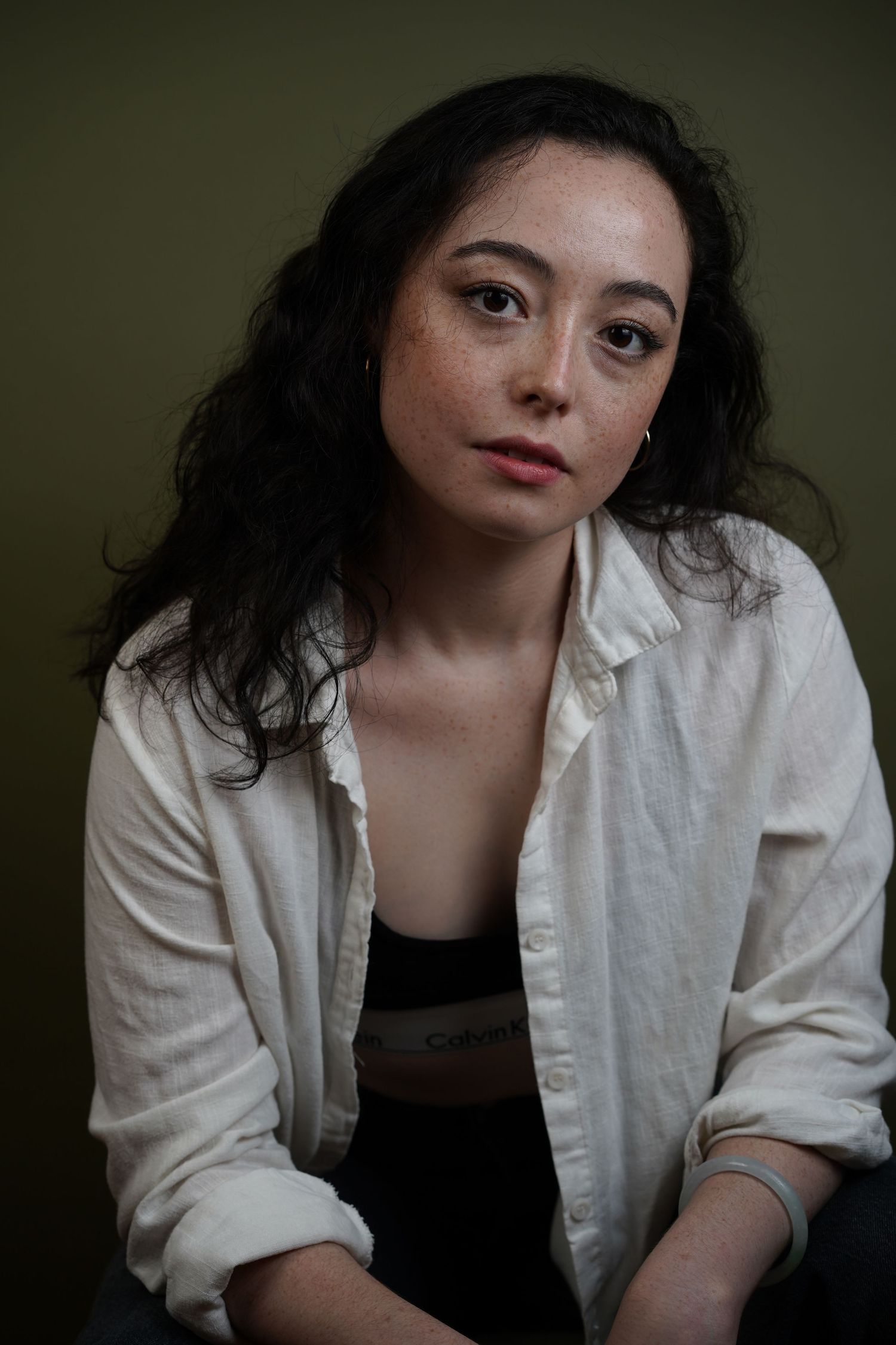 Portrait shot against dark background showing person in white button-down shirt and dark top with dramatic lighting.