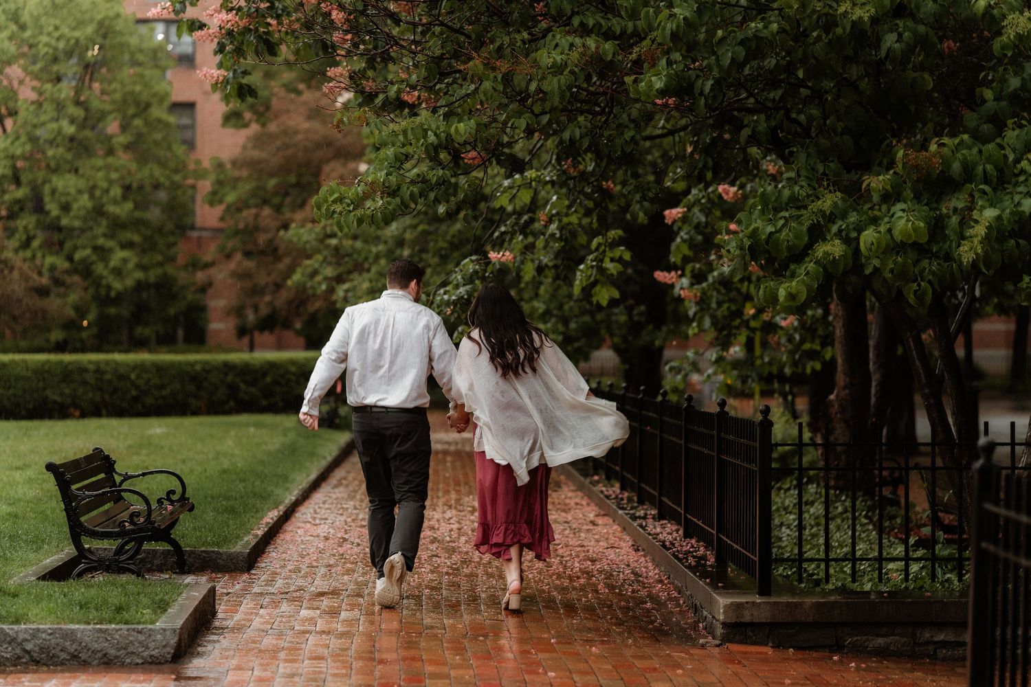 Couple walking hand-in-hand on a rainy brick path through a lush garden park.