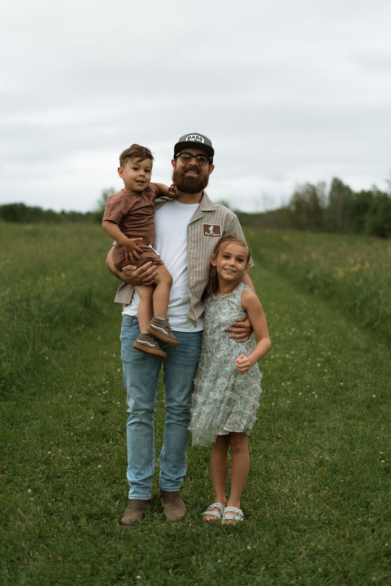 A parent and two children stand together in a green field on an overcast day.
