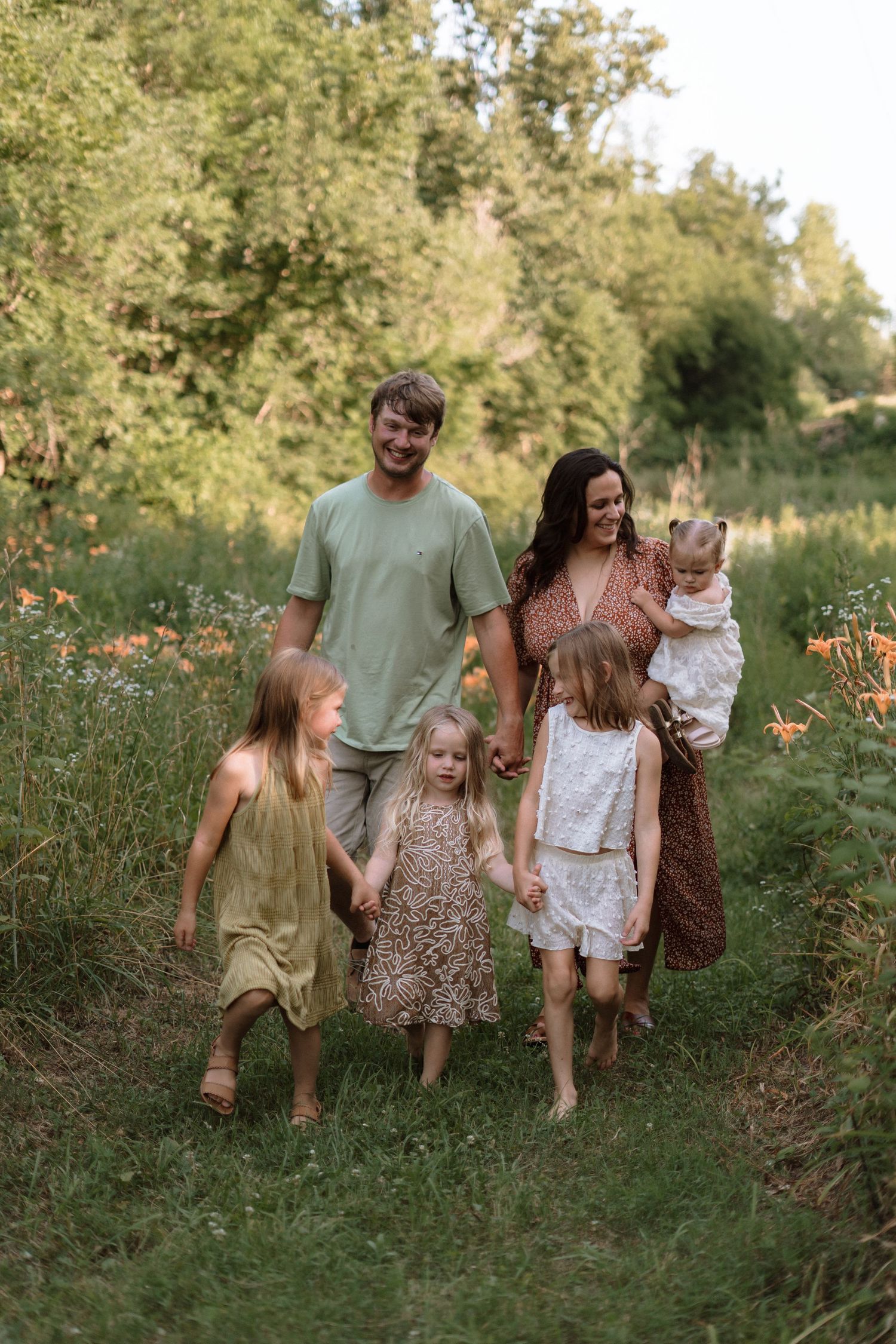 Family of six walking through a lush green meadow with orange wildflowers during golden hour.