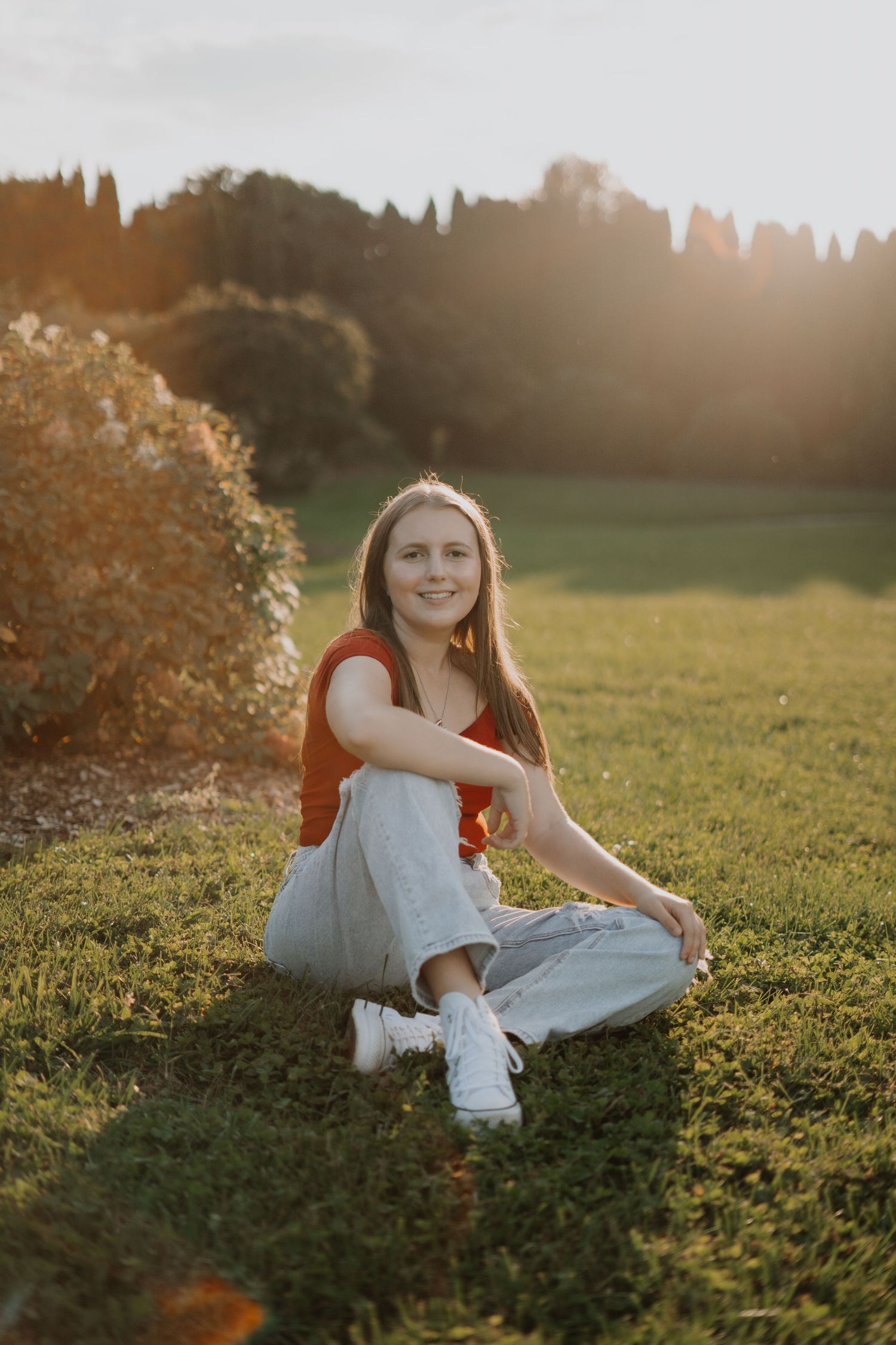 Senior portrait of person in casual attire sitting in sunlit grass field during golden hour.
