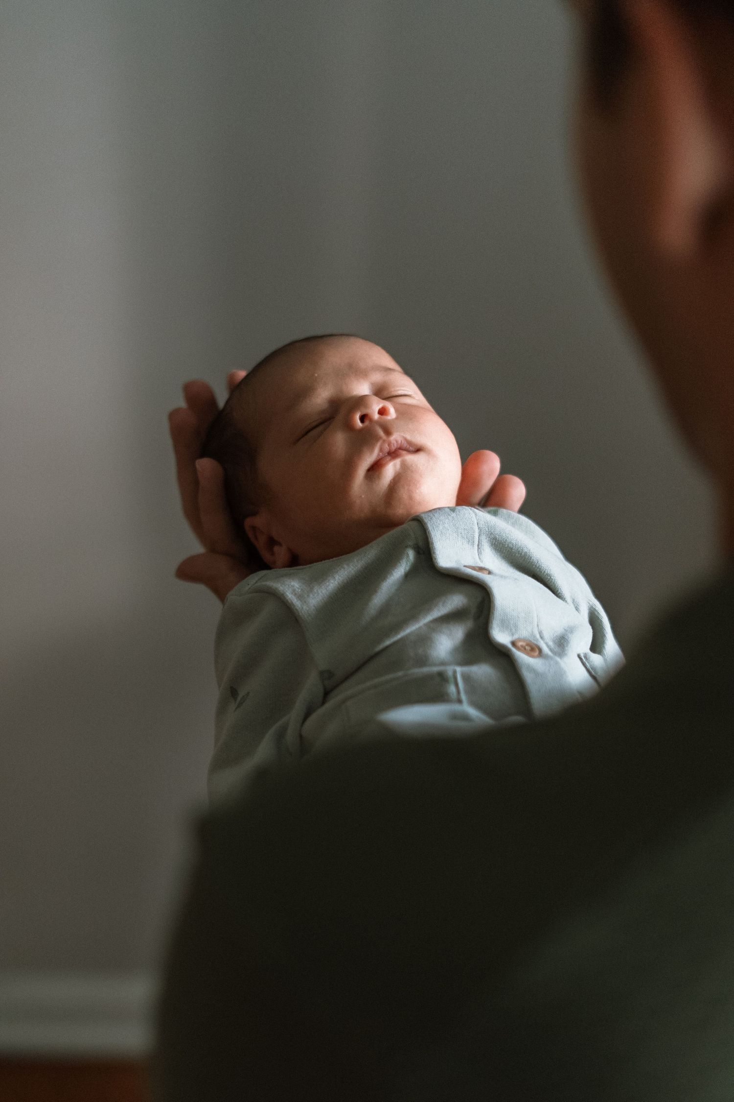 A sleeping newborn baby swaddled in light blue blanket being held against someone wearing dark green.
