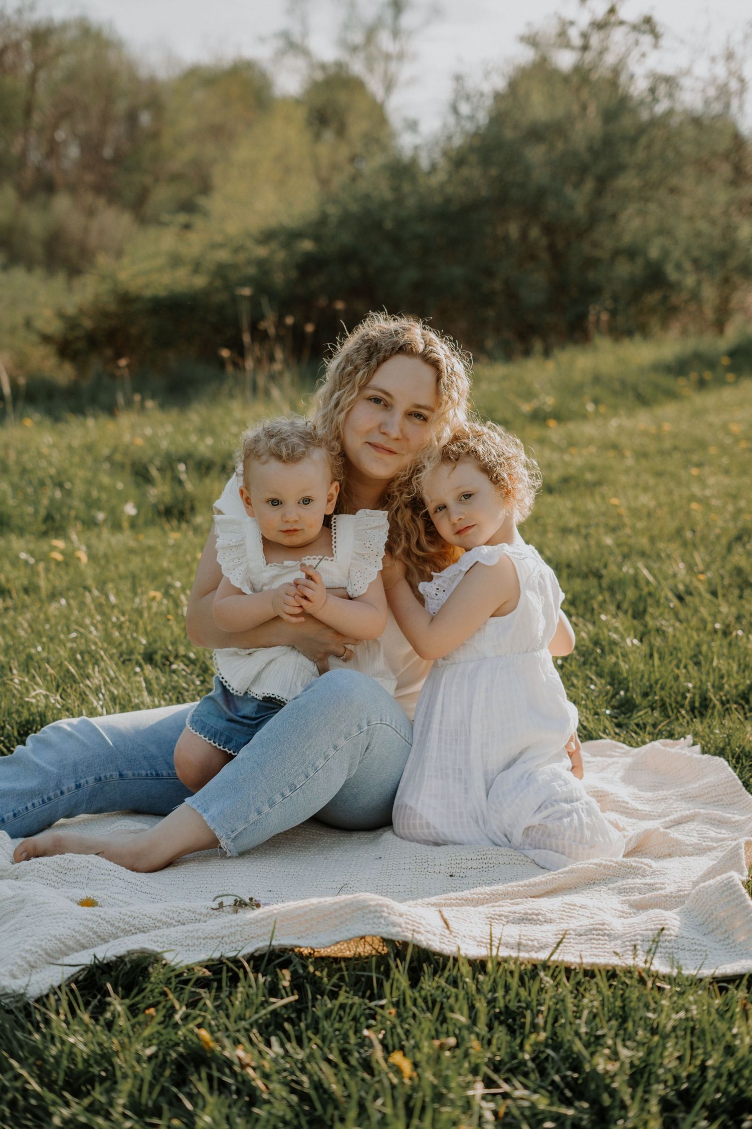 Mother and children share tender moments while sitting on blanket in sunny meadow.