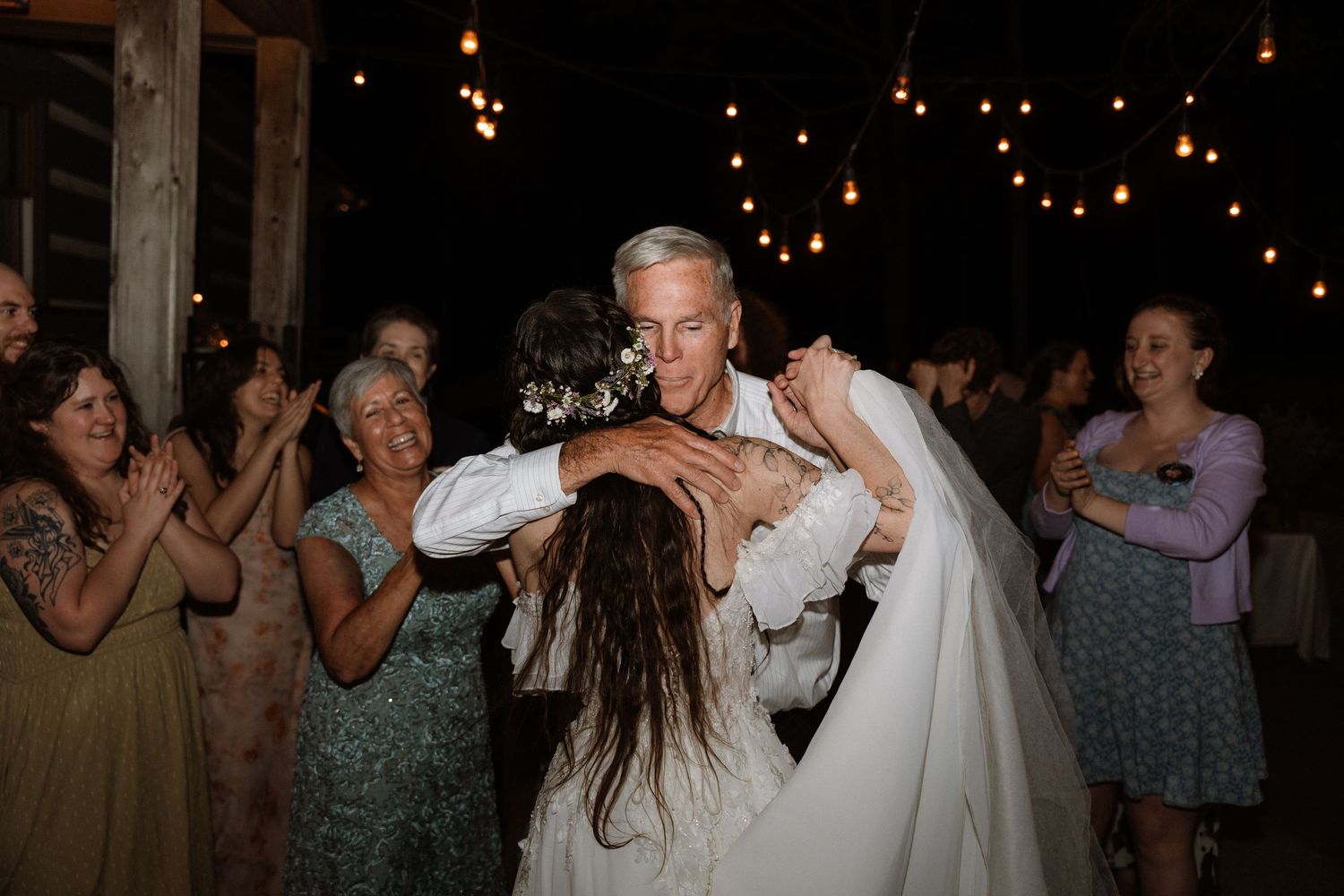 Bride and groom share a joyful embrace on the dance floor surrounded by guests at a romantic rustic wedding reception.