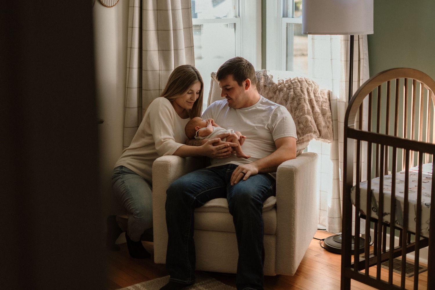 Parents share tender moments with their newborn baby in a softly lit nursery with a wooden crib.