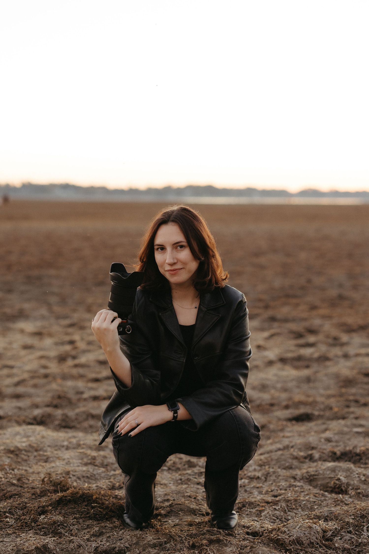 Person in black attire crouches in desert landscape at golden hour creating moody artistic portraits.