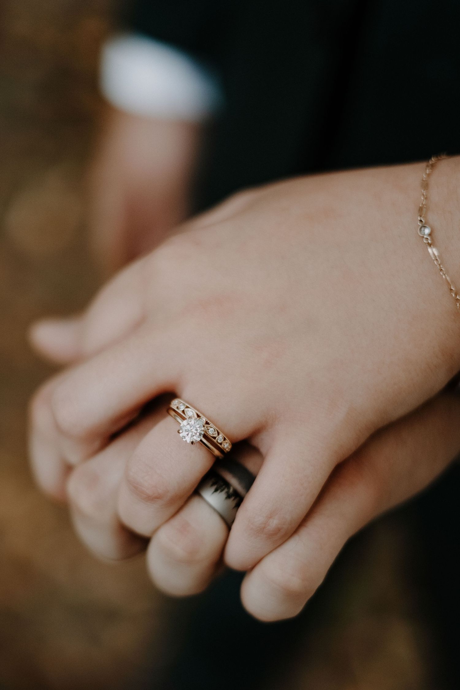 Close-up of engagement ring and wedding band on hand with delicate bracelet.