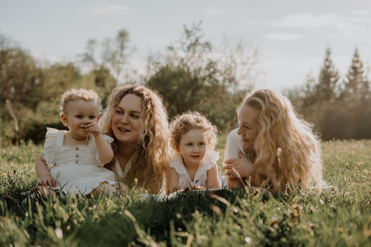 Candid family portrait of adults and children laying in sunny spring grass.