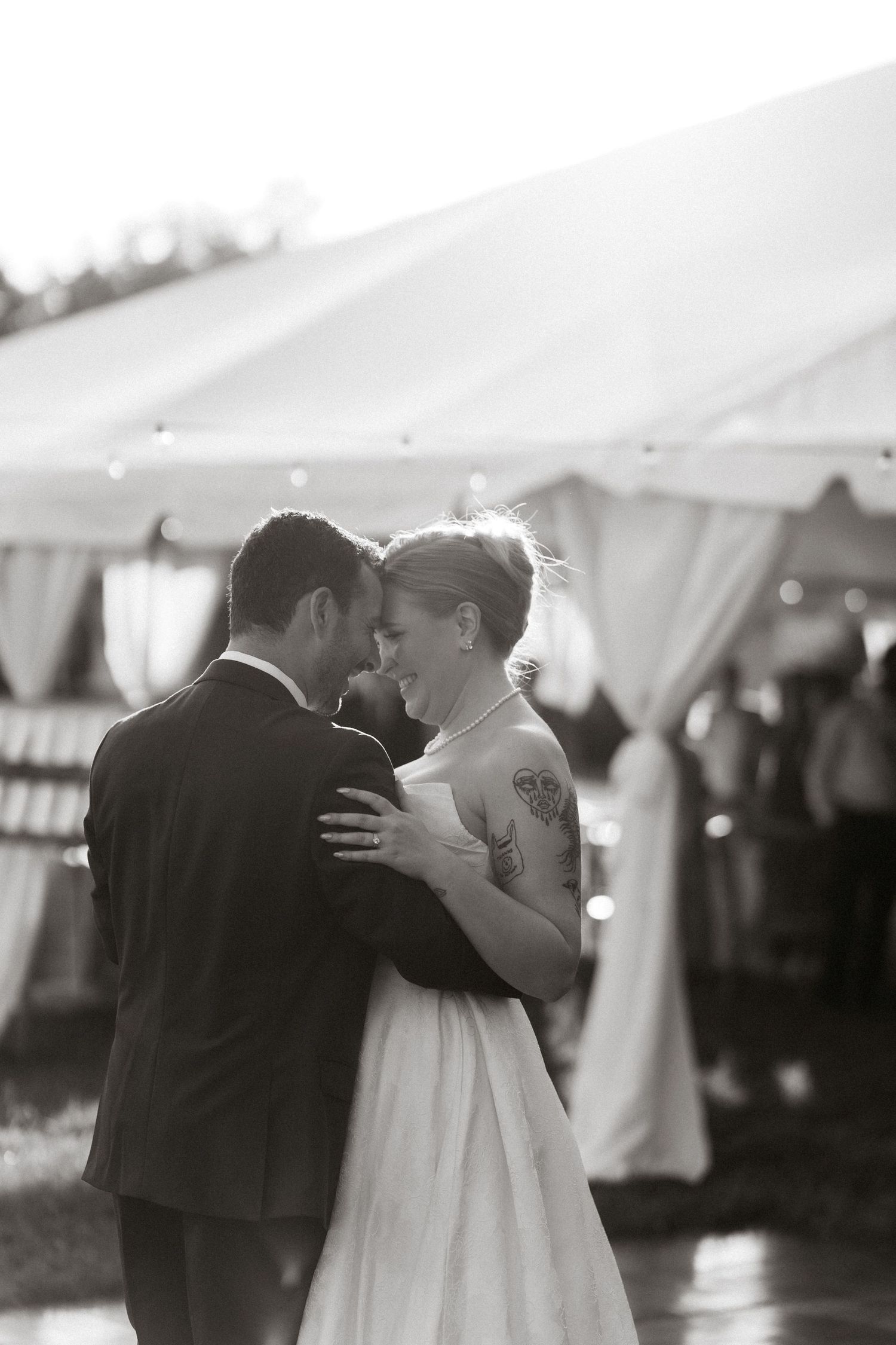 Black and white photo of a bride and groom sharing their first dance under a white tent at their wedding reception.