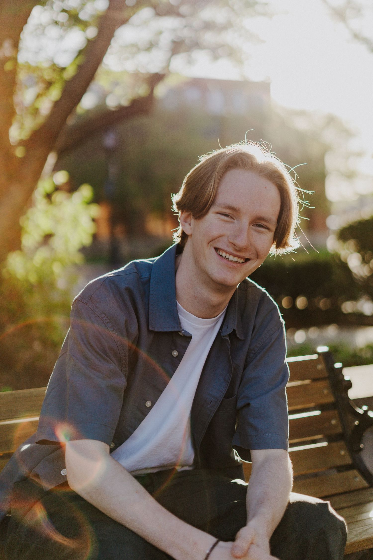 Senior portrait of a person sitting on a park bench smiling during golden hour sunset.