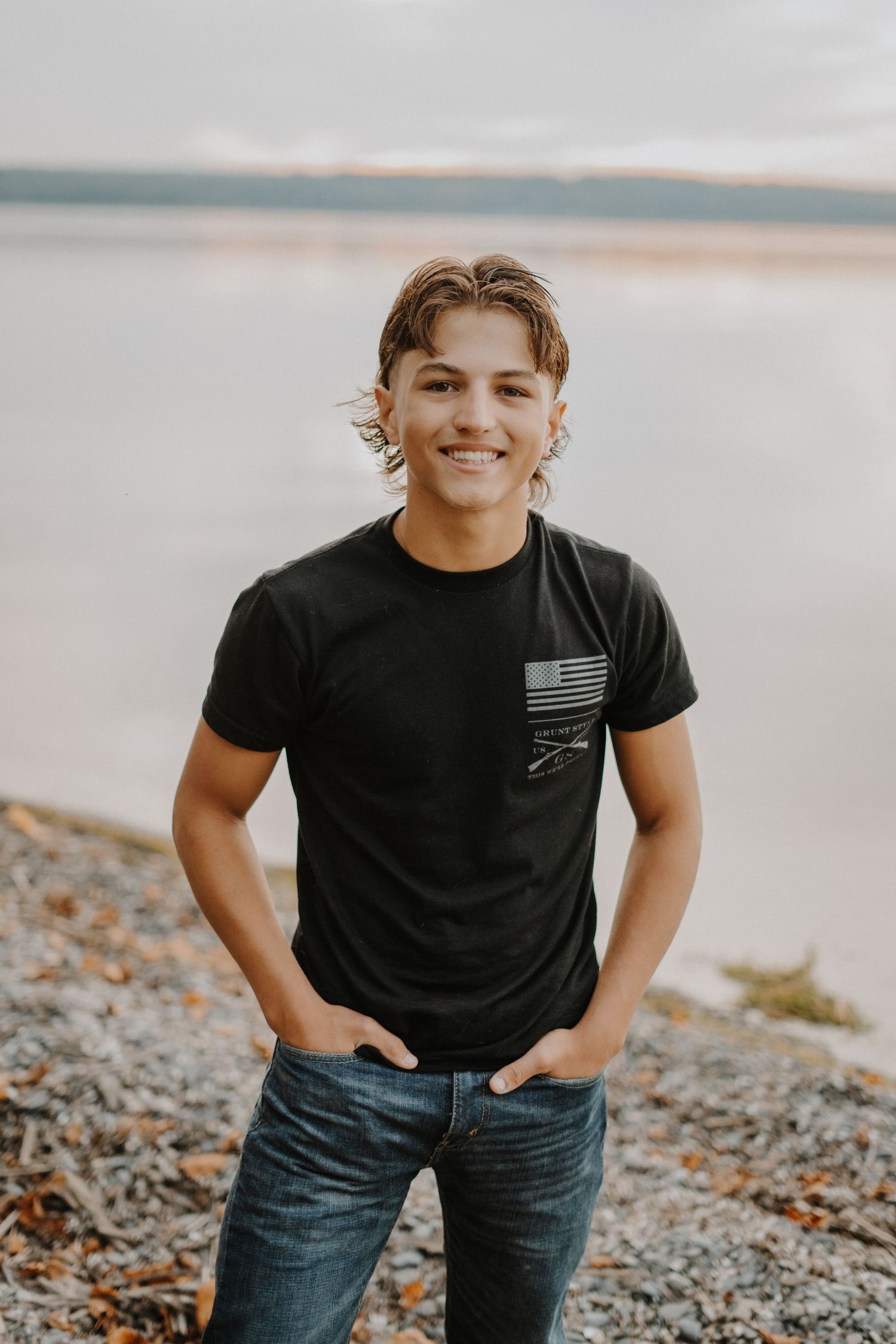 A senior portrait of someone wearing a patriotic t-shirt against a serene lakeside backdrop.