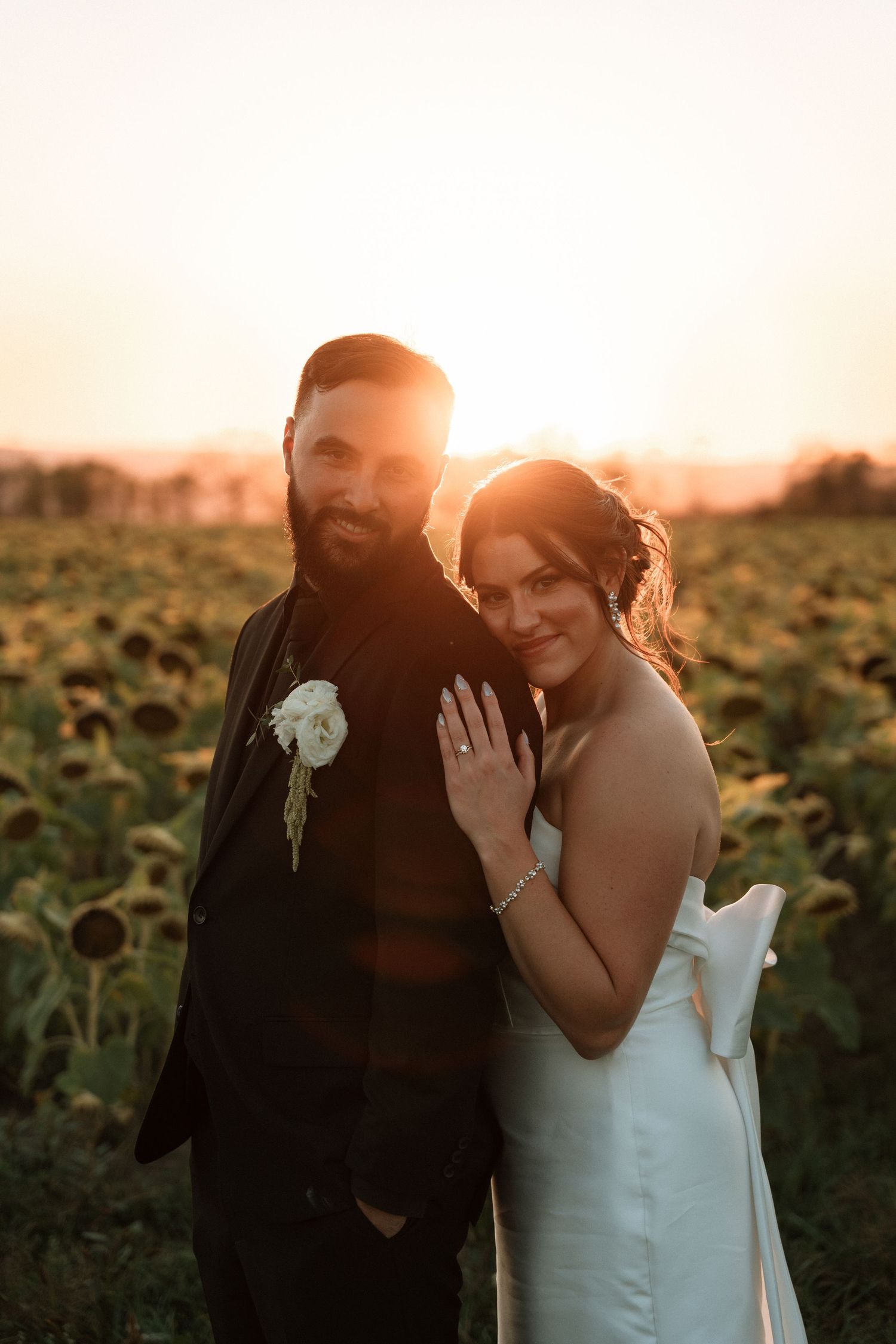 A couple shares a romantic moment at sunset in a sunflower field wearing wedding attire.