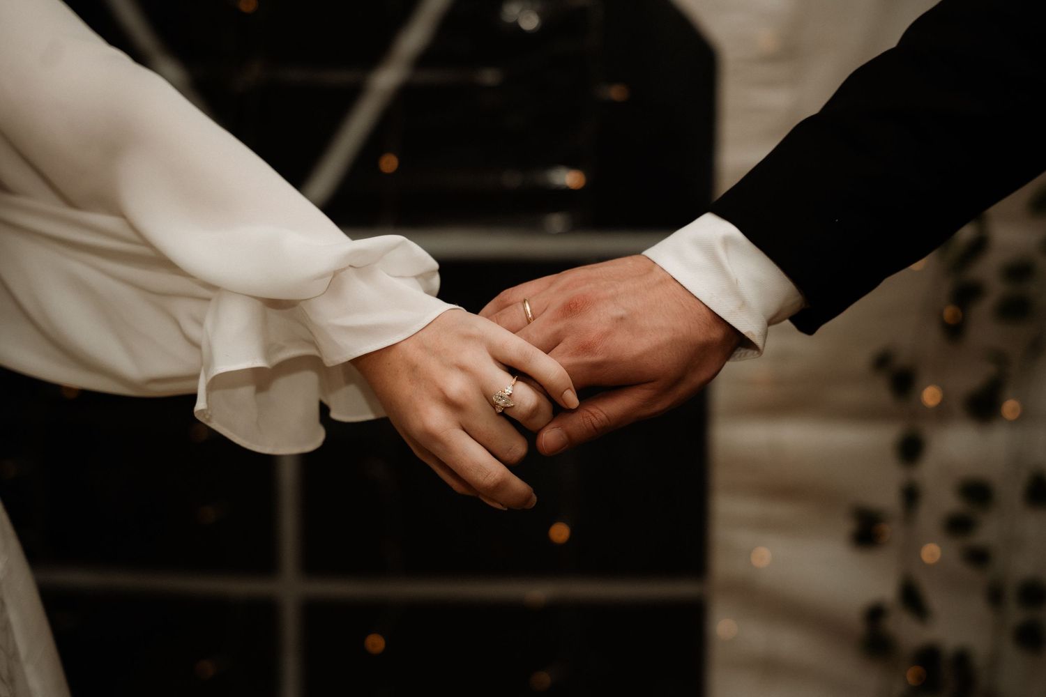 Close-up of hands exchanging wedding rings during an intimate ceremony in low light.