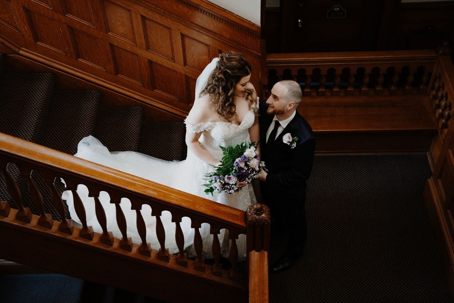 A couple shares an intimate moment on wooden stairs in a dark interior setting.
