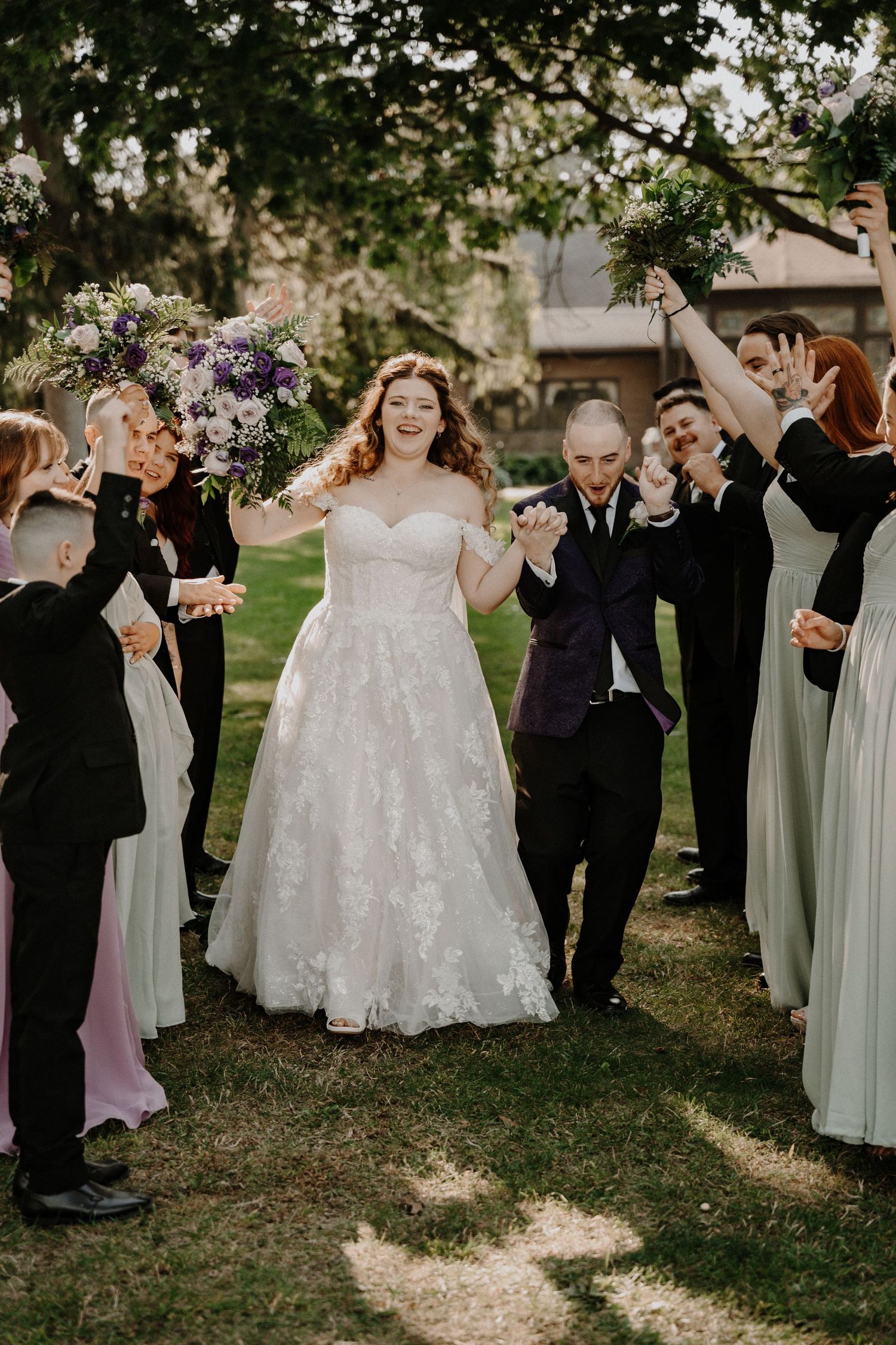 Wedding celebration with guests cheering as newlyweds walk between them on garden path.