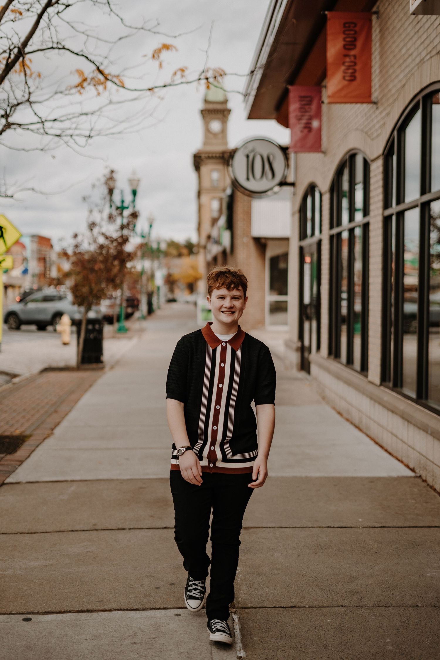 Senior portrait of person walking along downtown sidewalk with historic buildings and clock tower visible.