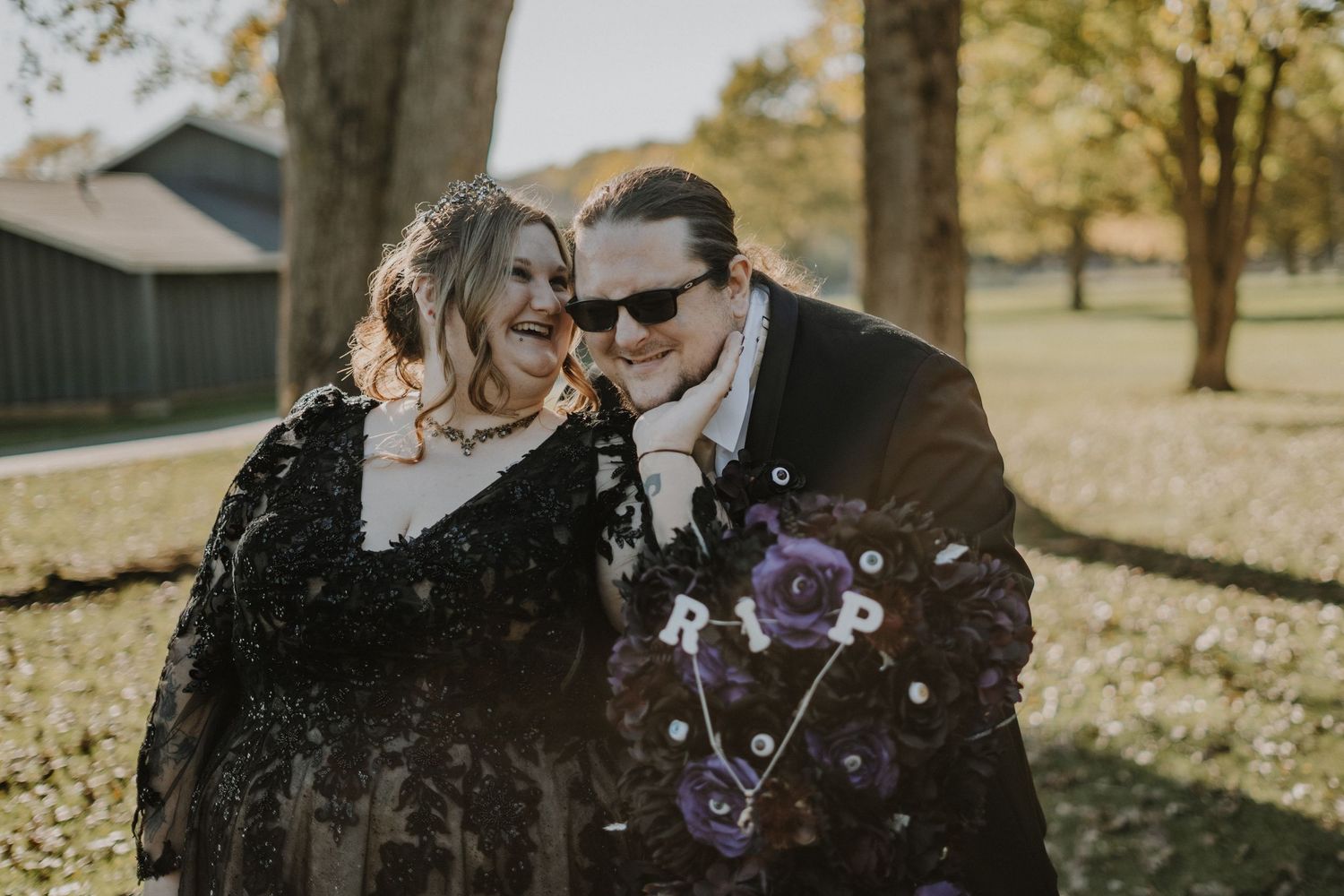 A candid wedding portrait of a couple laughing together while holding a purple bouquet in fall scenery.