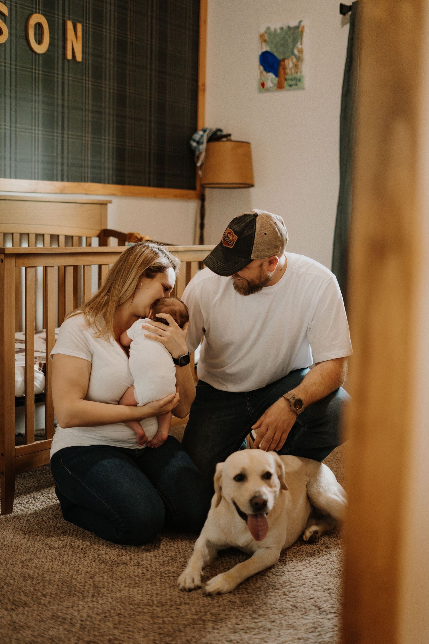 A family and their white dog share an intimate moment in a nursery room with a crib.