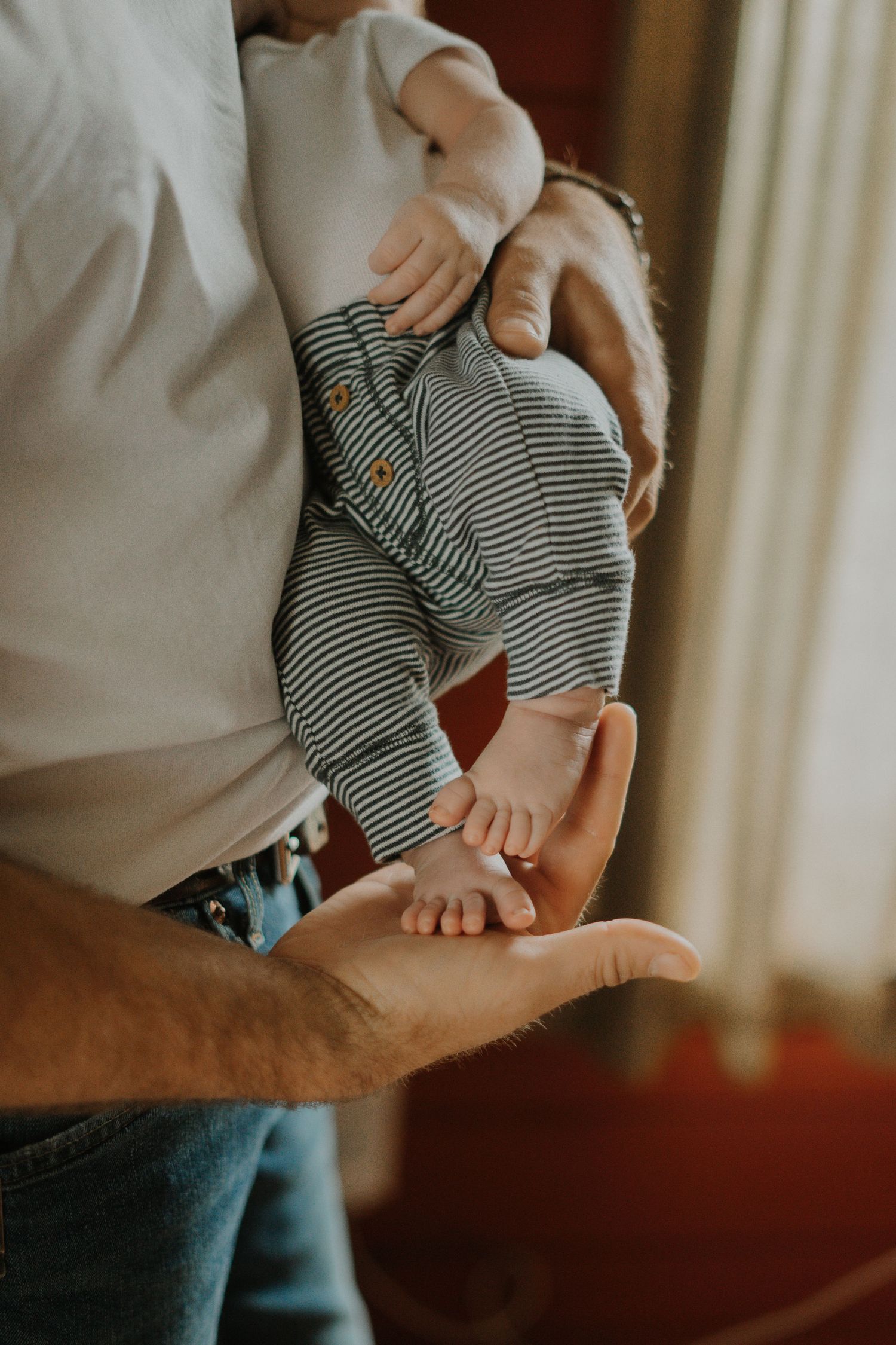 A baby in striped clothing is held gently in someone's hands, showing tiny bare feet.