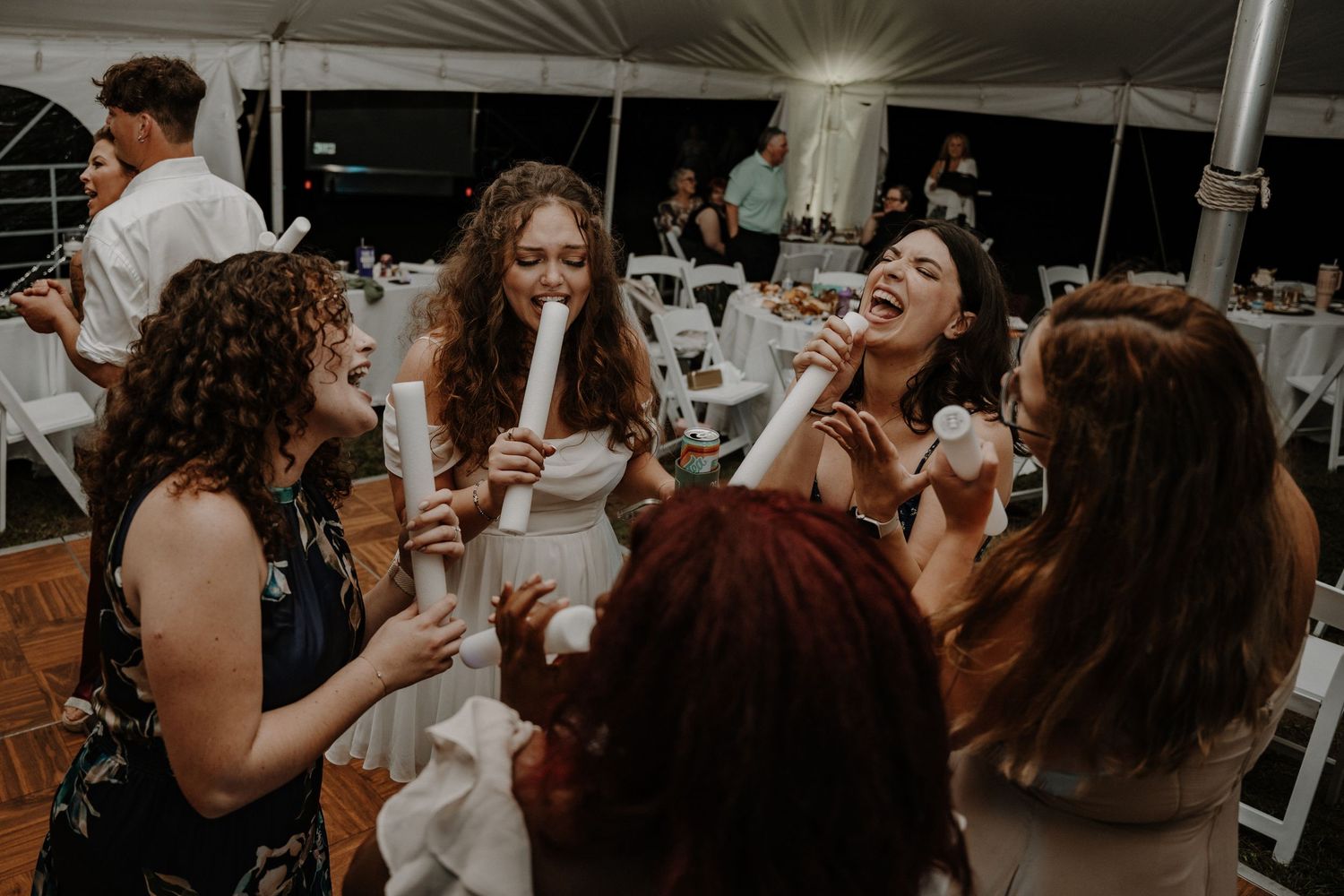 Group of wedding guests laughing and enjoying drinks under tent reception.