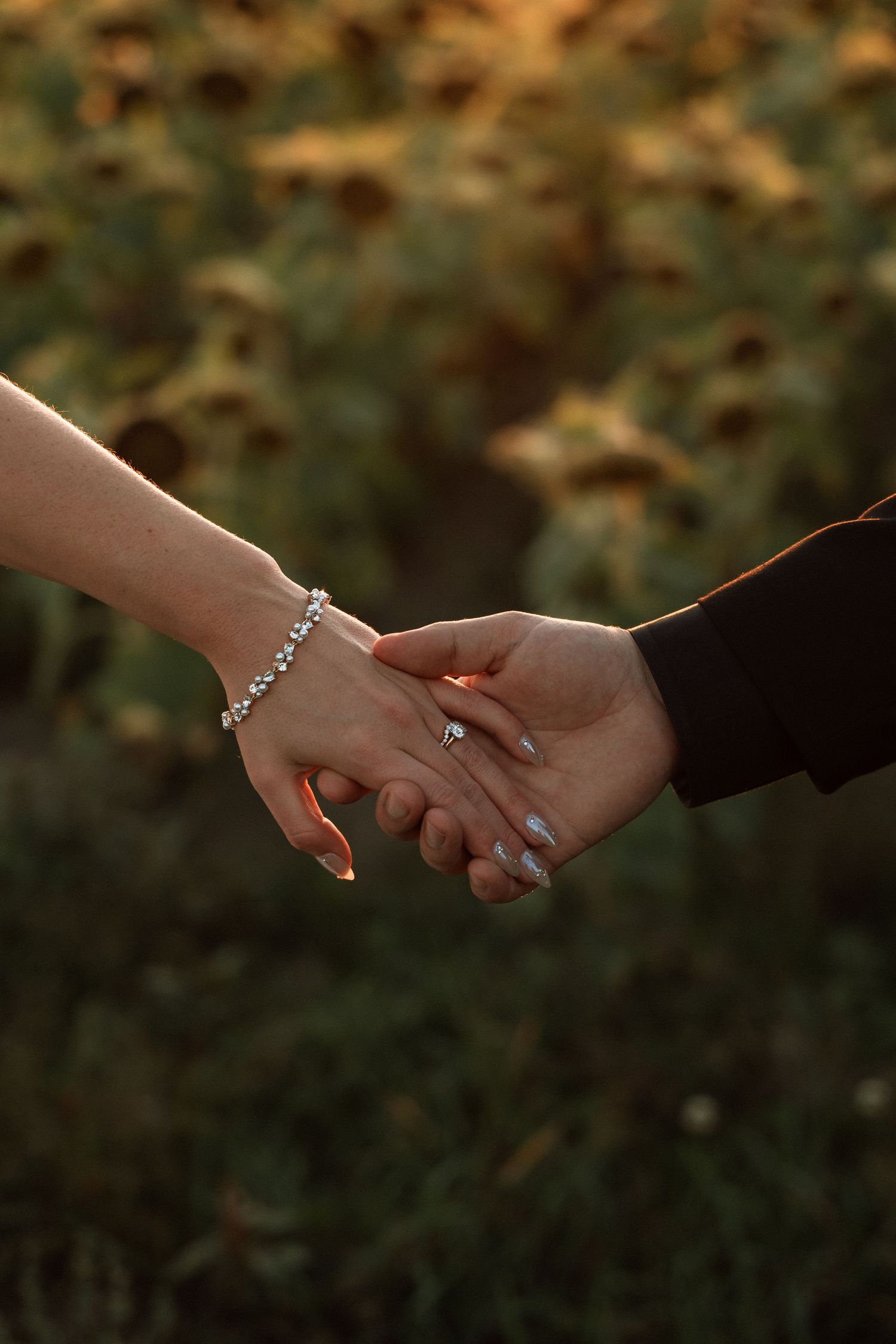 Close-up view of hands holding each other with engagement ring in romantic outdoor setting during golden hour.