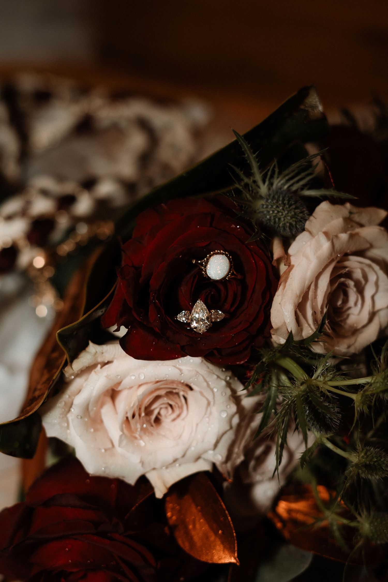 Deep burgundy and blush pink roses with delicate pearl accents create a romantic floral arrangement in moody lighting.
