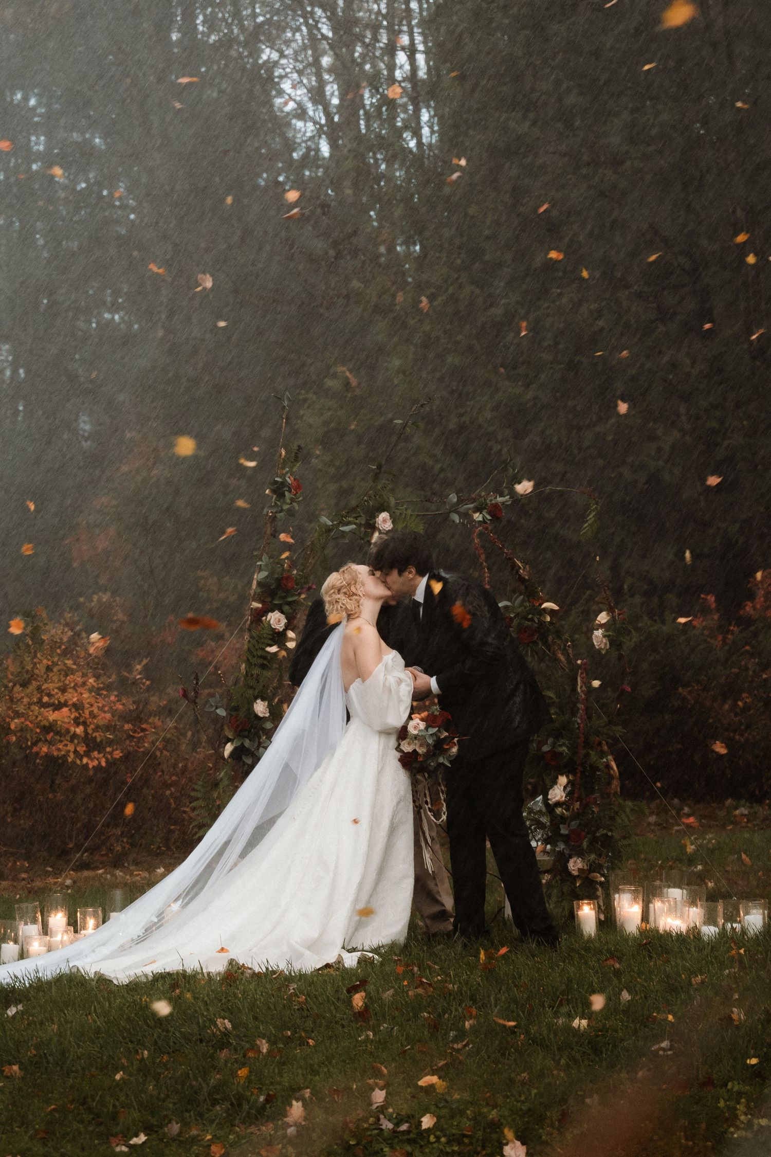 Wedding party celebrates outdoors as autumn leaves swirl through the air during a magical fall ceremony.