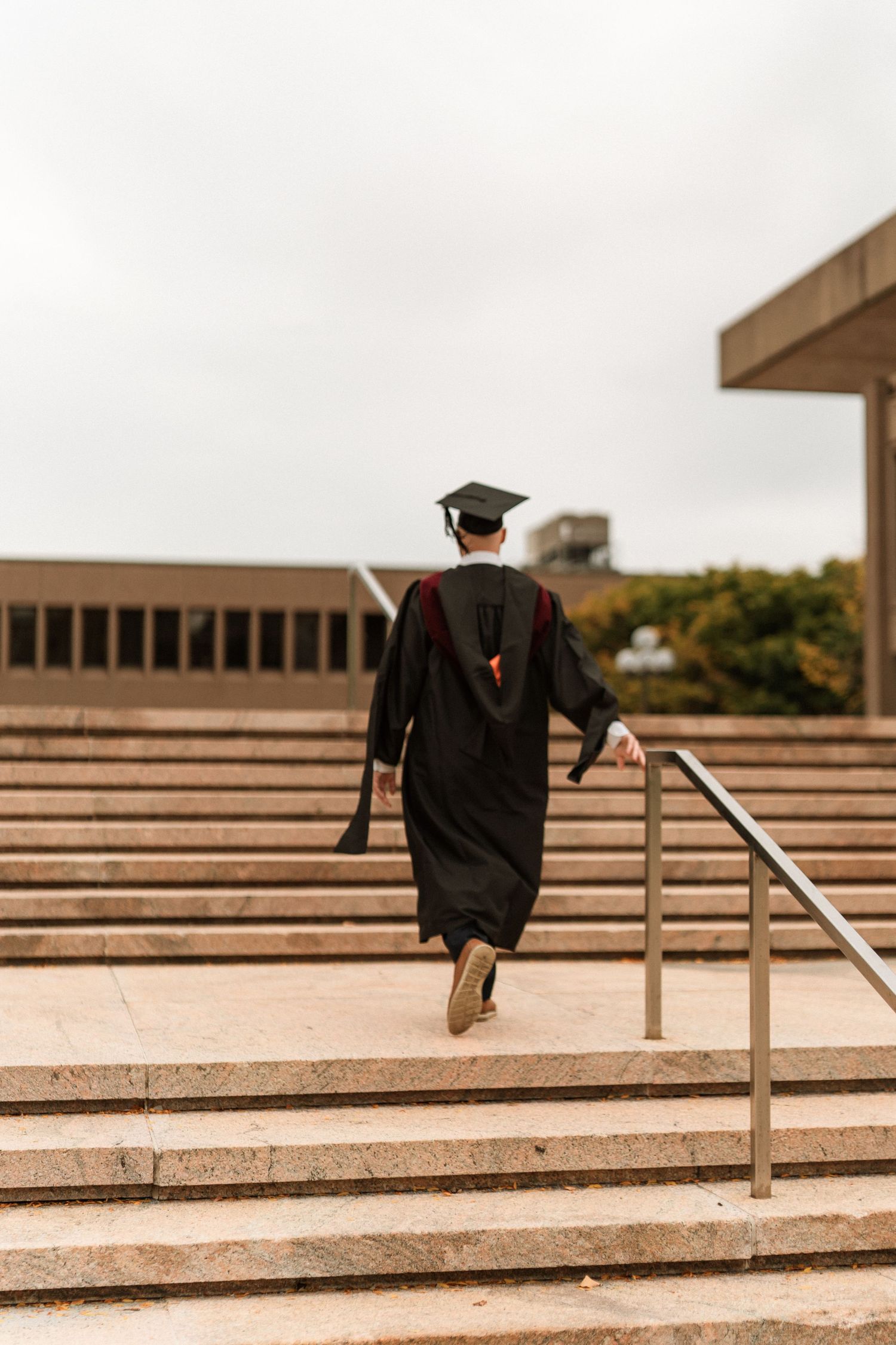 Graduate in cap and gown walks across concrete steps in a panoramic sequence of motion.