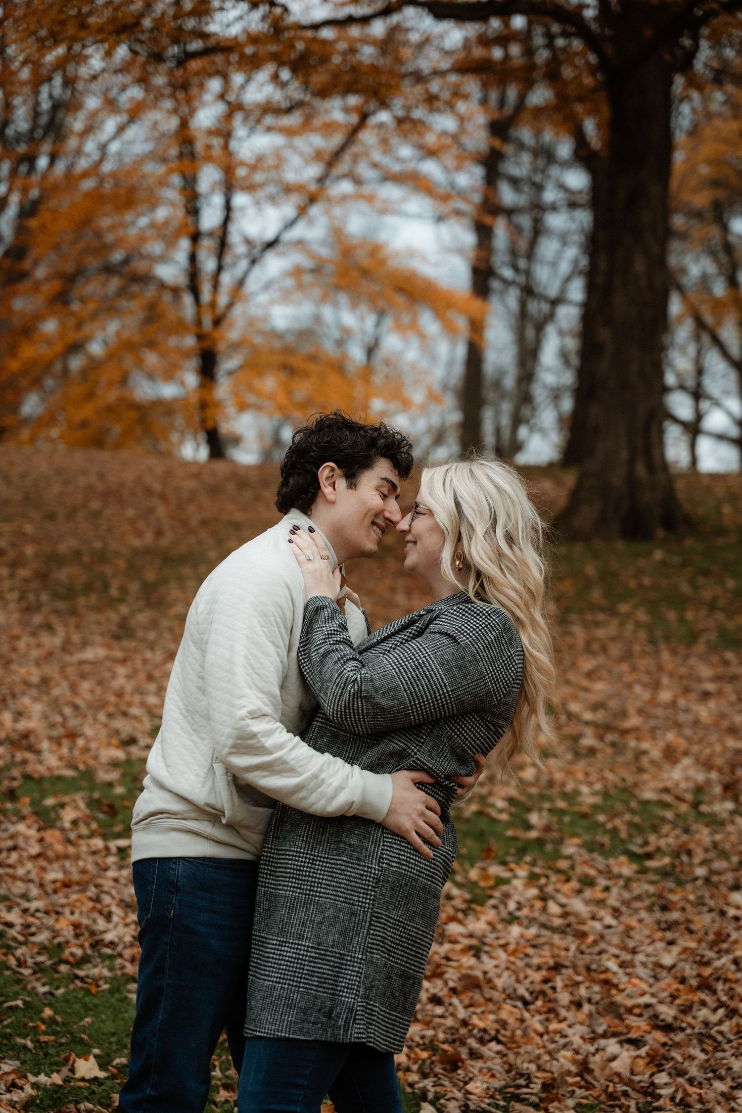 Couple sharing a romantic almost-kiss embrace outdoors among vibrant orange autumn leaves and trees.